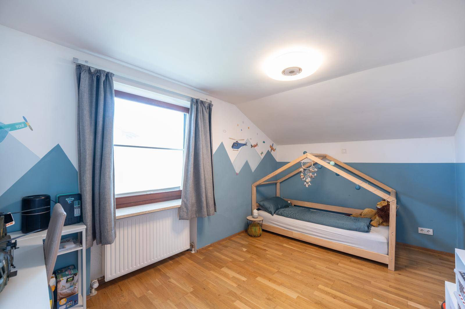 Kinderzimmer mit Holzboden, farbenfroher Wandgestaltung und Fenster, ideal für kleine Abenteurer.