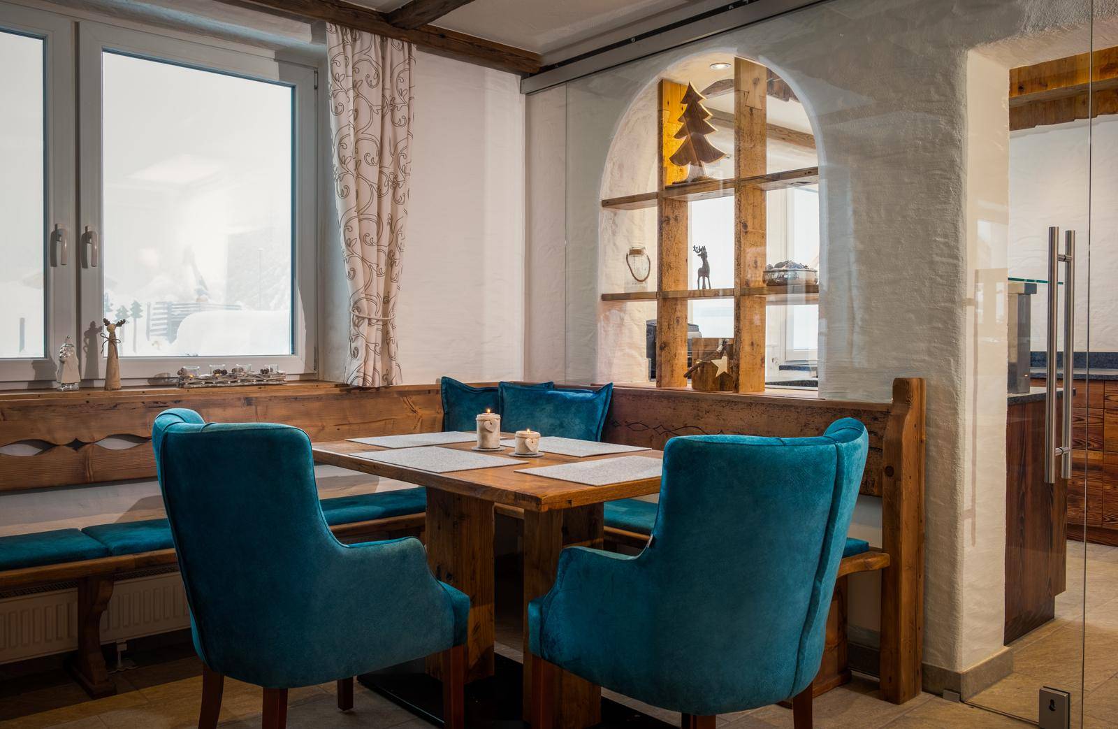Gemütlicher Essbereich im alpinen Stil mit Holztisch, blauen Stühlen und Fensterblick.