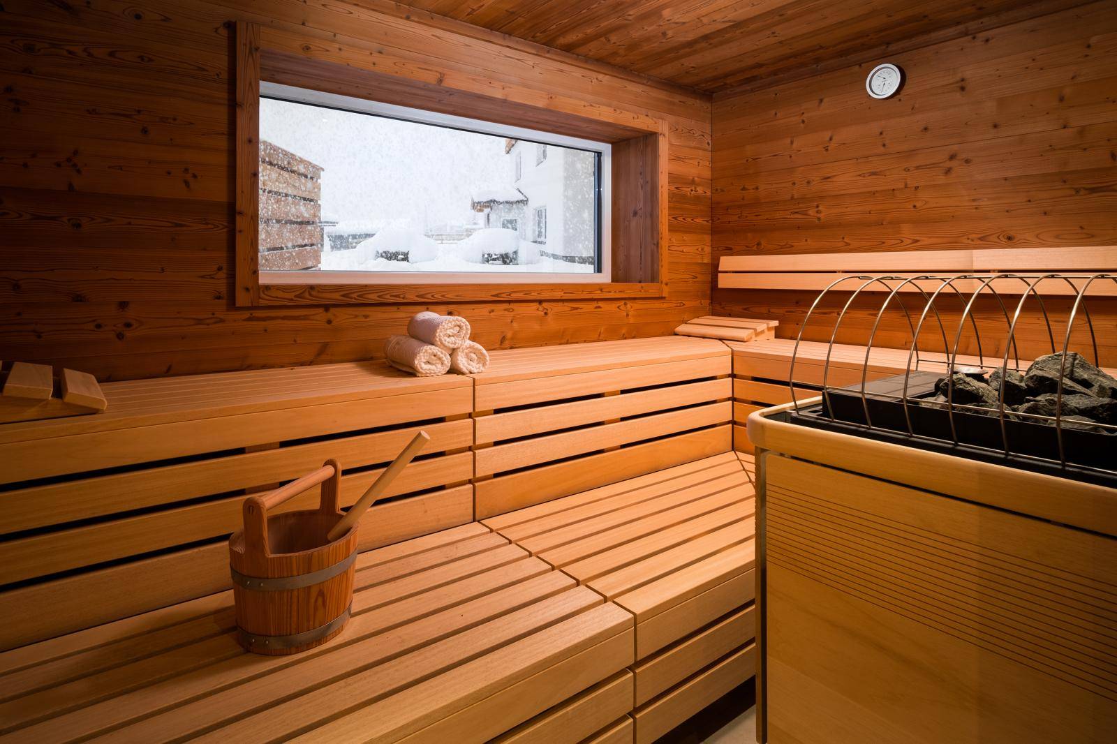 Holzsauna mit Bänken, Saunaofen und Fensterblick auf die verschneite Außenwelt.