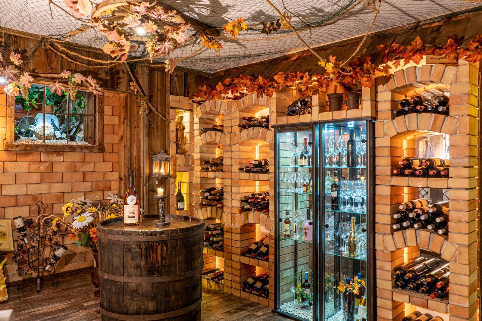 Rustikaler Weinkeller mit Ziegelgewölben, Holzfass und beleuchtetem Weinkühlschrank.