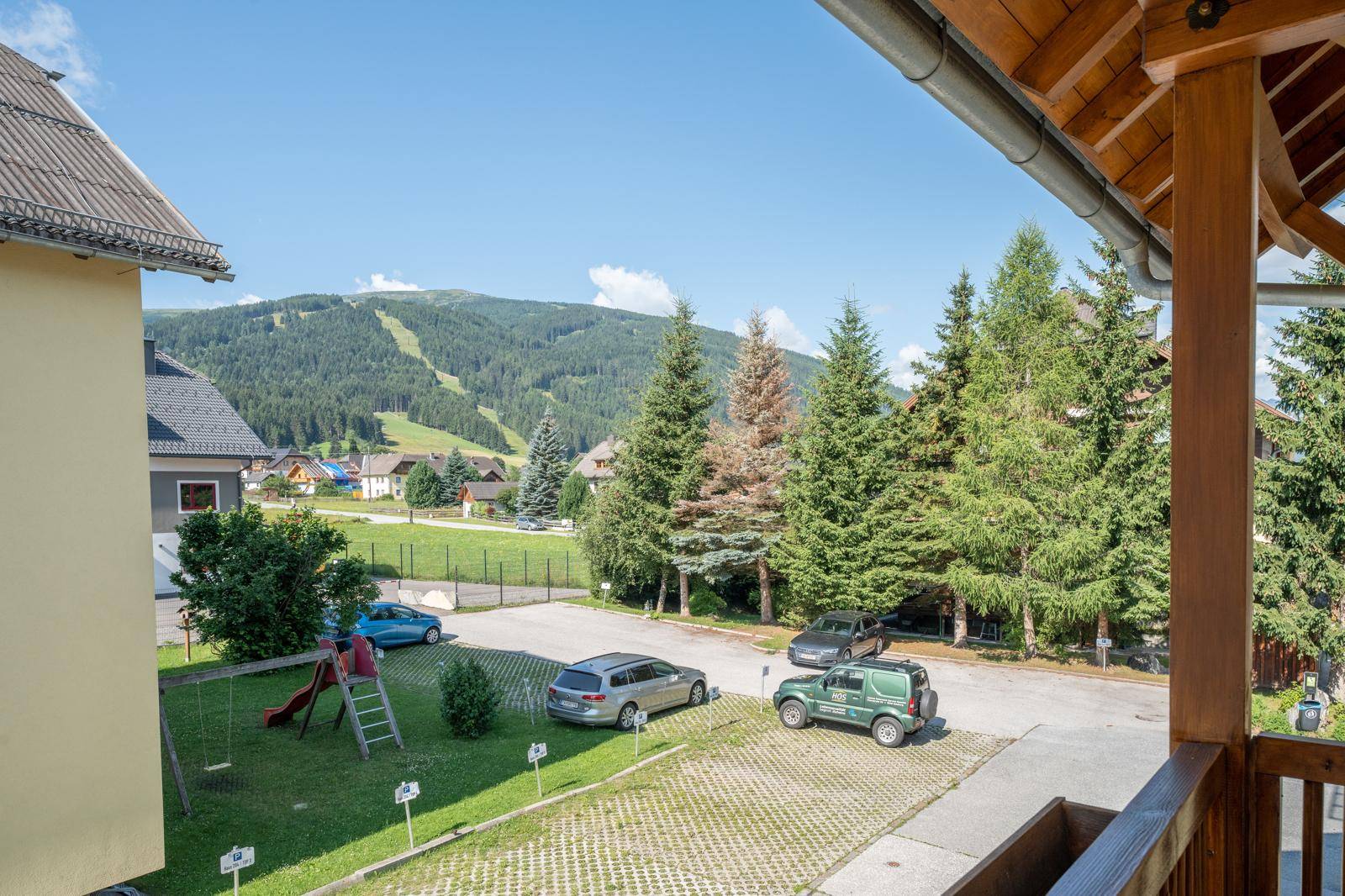 Außenbereich mit Spielplatz, Parkplätzen und Bergblick im Hintergrund.