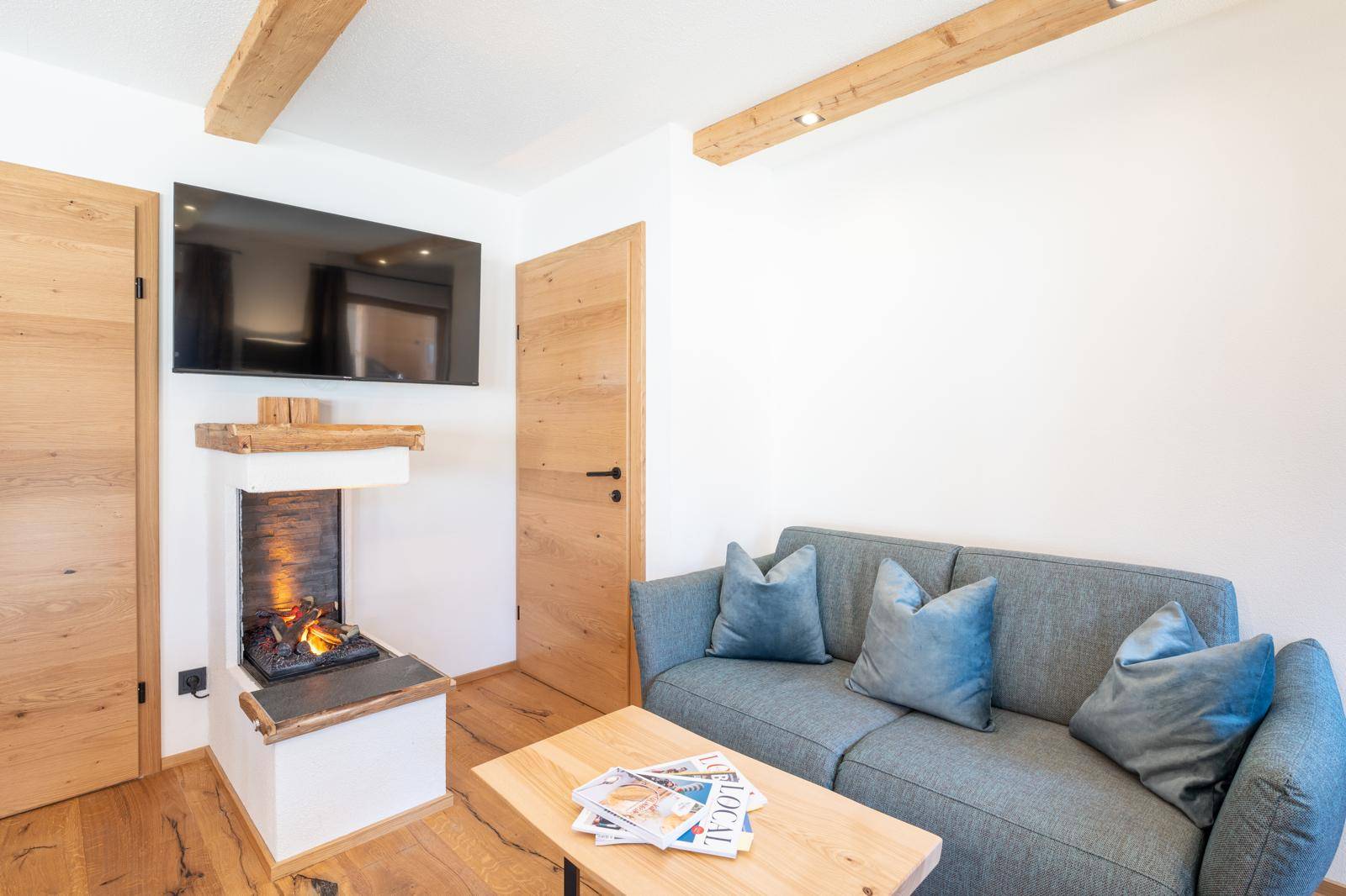 Gemütlicher Wohnbereich mit Sofa, Holzboden und modernem Kamin unter einem Fernseher.