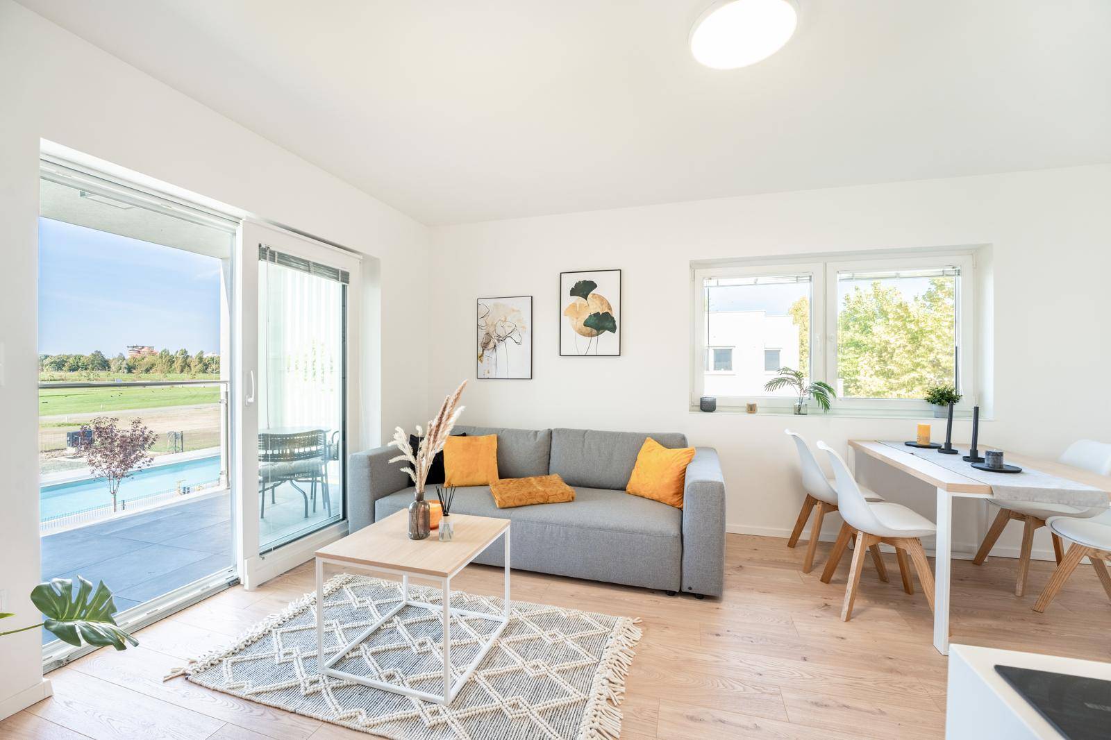 Helles Wohn-Esszimmer mit Holzboden, bequemer Couch und Zugang zur Terrasse mit Poolblick.