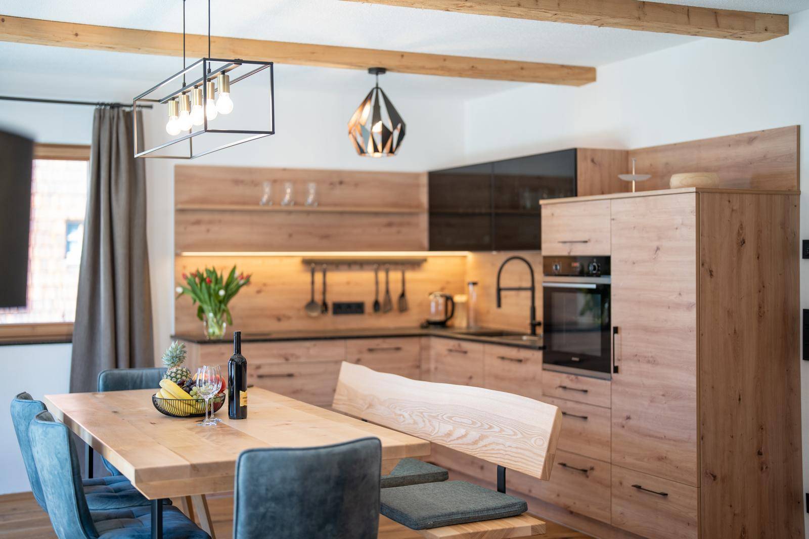 Stilvolle Holzküche mit dunkler Arbeitsplatte, modernen Hängelampen und Essbereich.