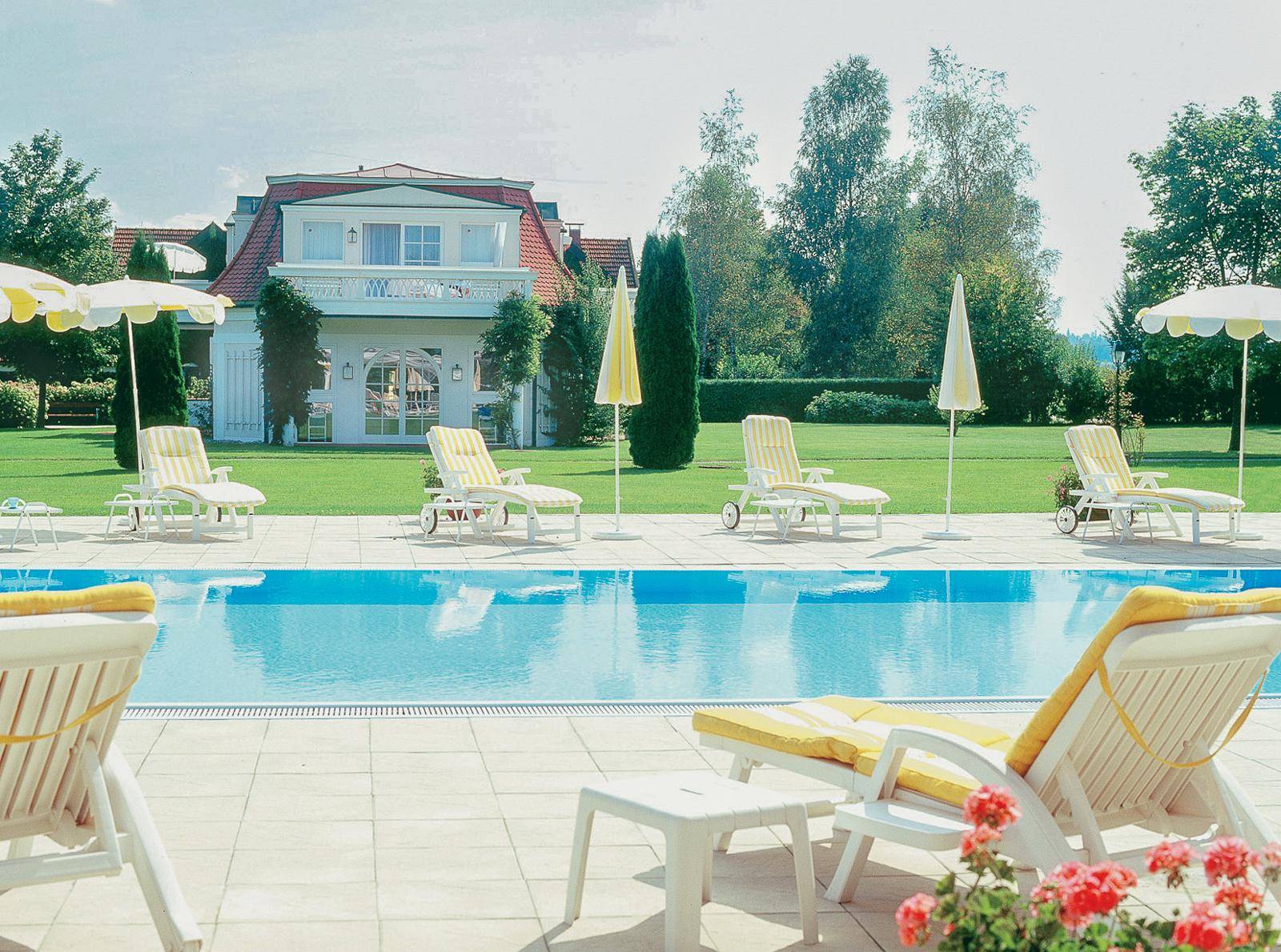 Außenpoolbereich mit Liegestühlen, Sonnenschirmen und Blick auf die elegante Villa.
