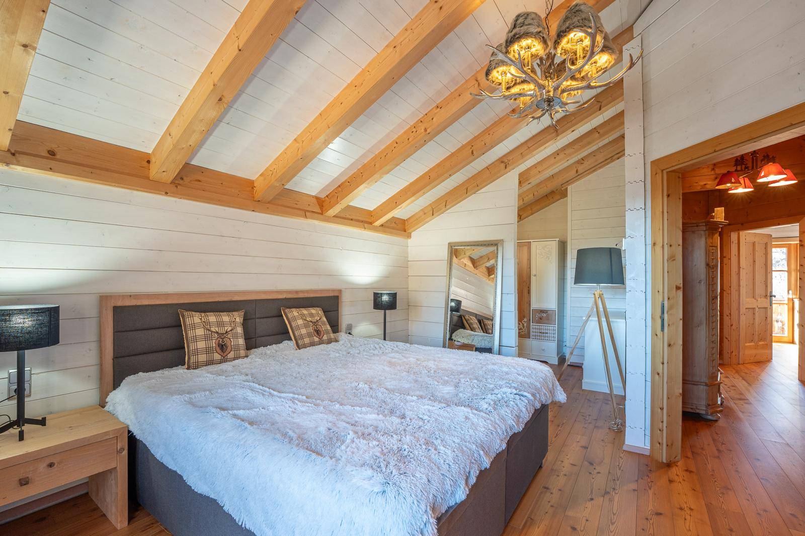 Geräumiges Schlafzimmer mit Holzbalkendecke, Holzboden und großem Bett im alpinen Stil.