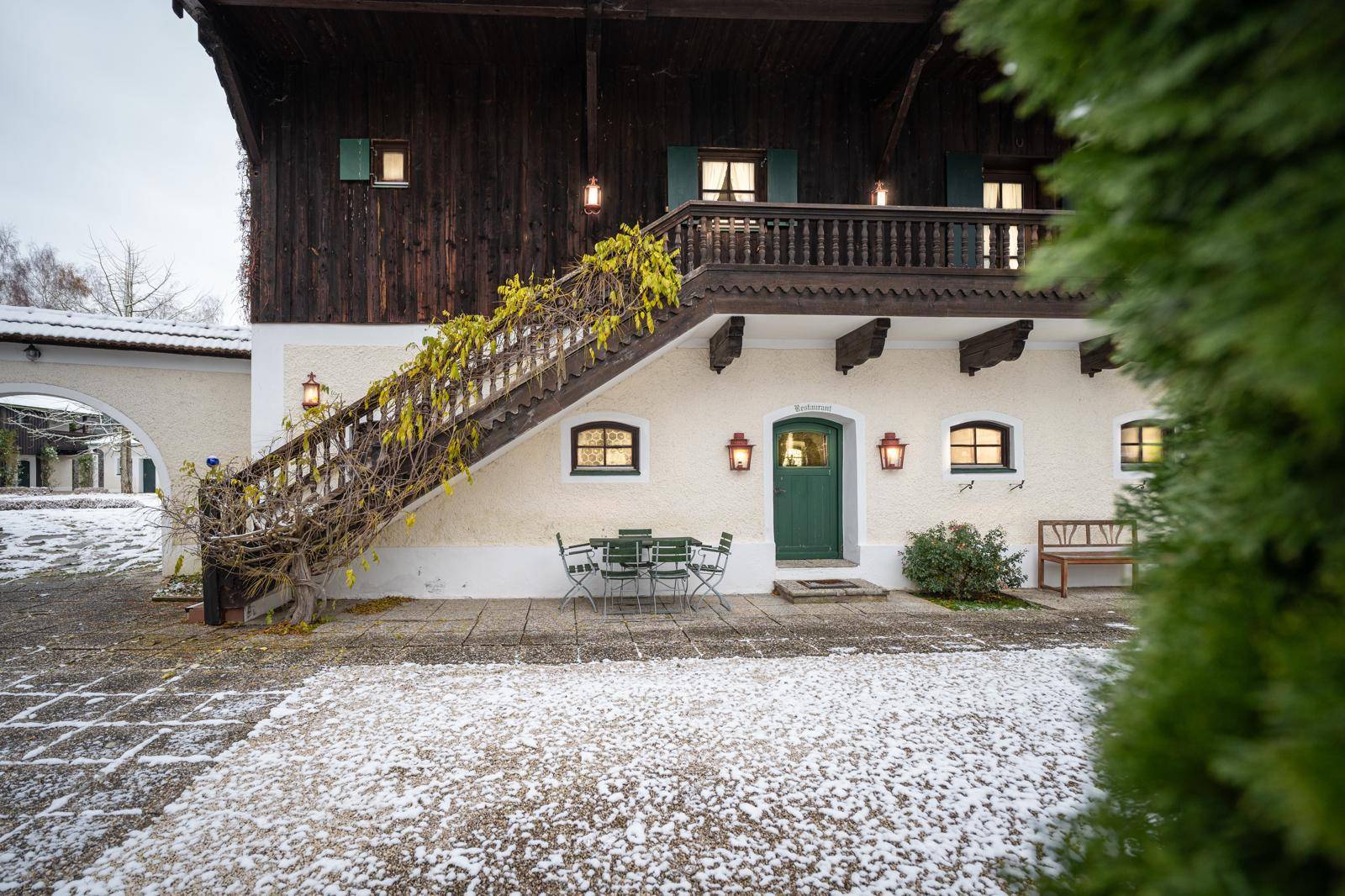Traditionelles Gebäude mit Außentreppe, Laternen und Sitzbereich im verschneiten Hof.