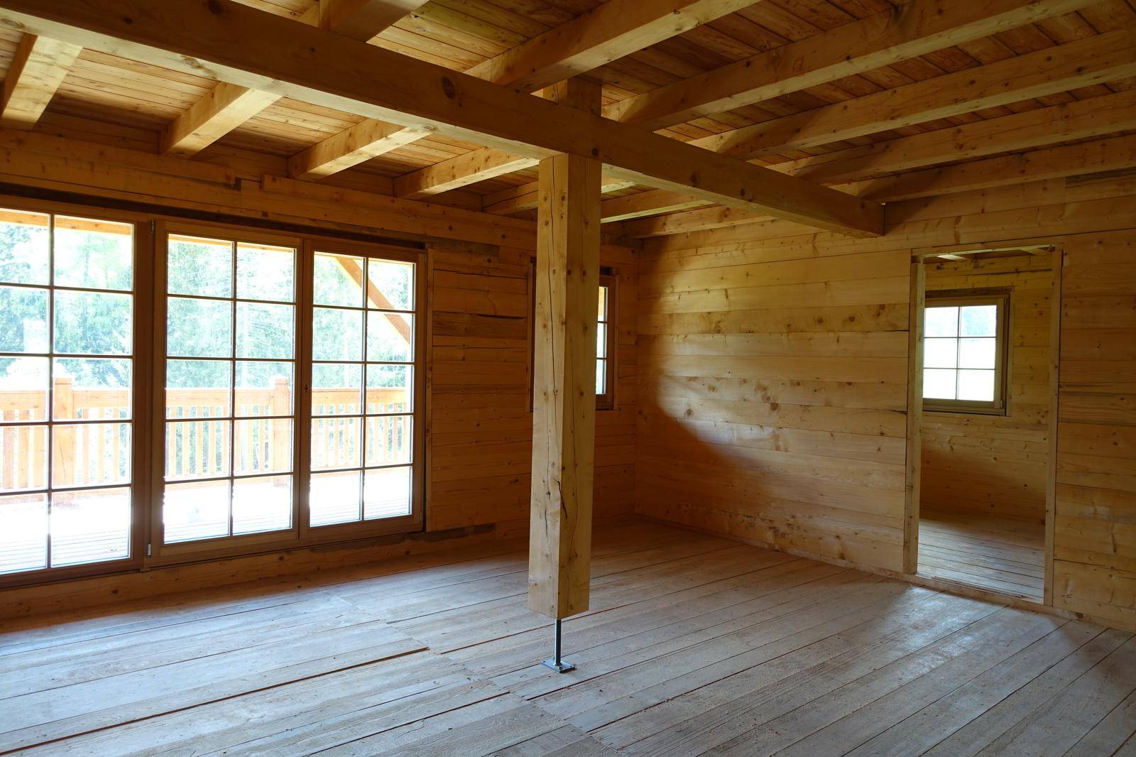 Unfertiger Innenraum mit Holzbalkendecke, Holzwänden und großen Fenstern.