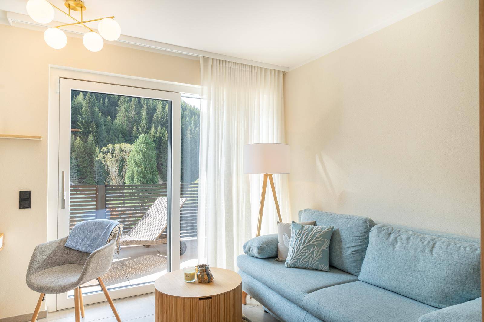 Gemütliches Wohnzimmer mit Sofa, Sessel und Zugang zu einem sonnigen Balkon.