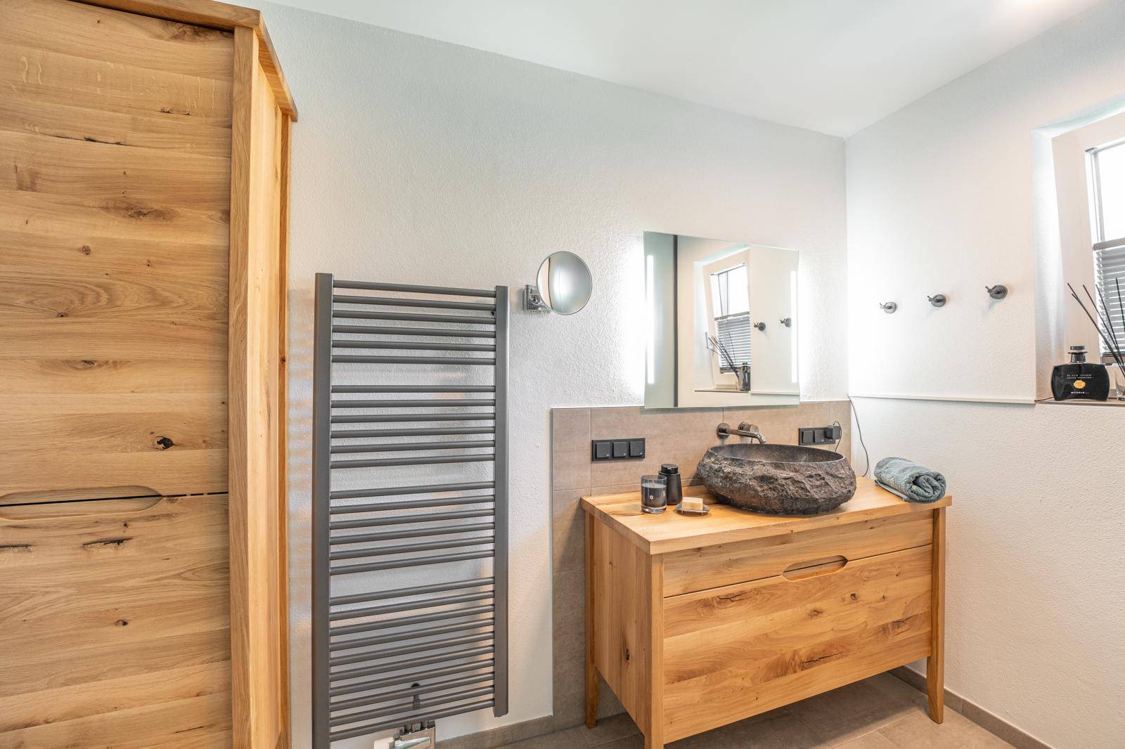 Stilvolles Badezimmer mit Holzwaschtisch, Natursteinbecken und beheiztem Handtuchhalter.