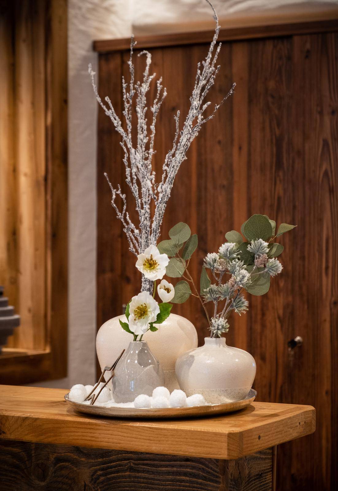 Nahaufnahme einer winterlichen Dekoration mit weißen Blumen und Zweigen auf einem Holztresen.