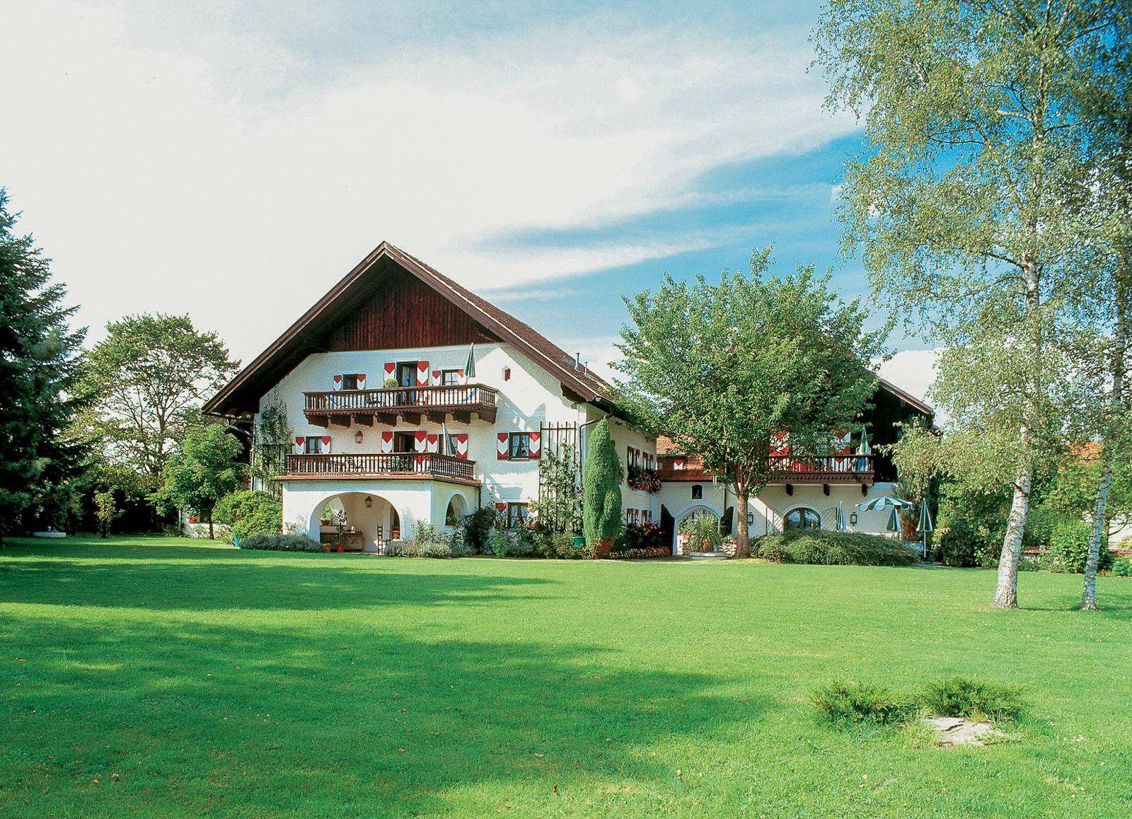 Weitläufiger Garten mit großer Rasenfläche und traditionellem Landhaus im Hintergrund.