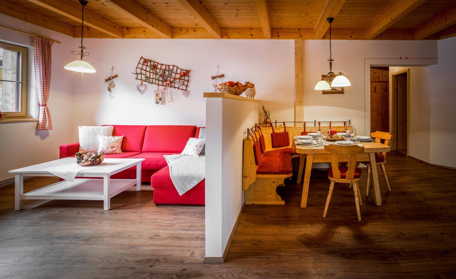 Gemütlicher Wohn-Essbereich mit rotem Sofa, Holzbalkendecke und rustikalem Esstisch.