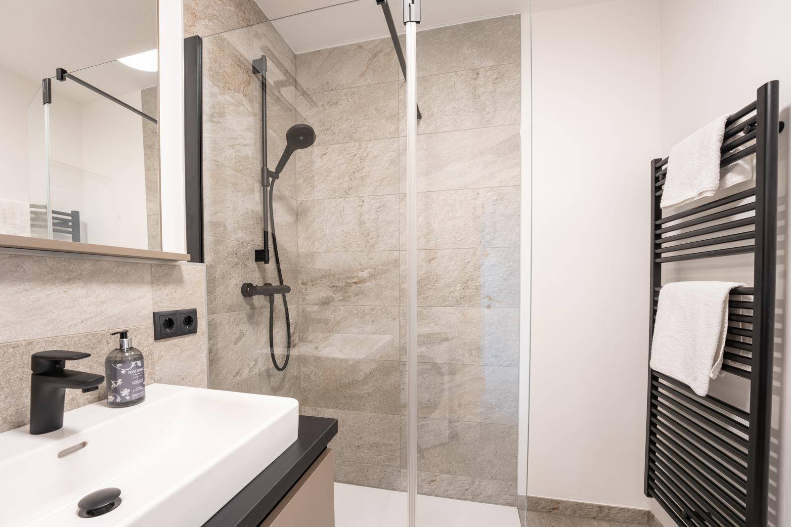Detaillierte Ansicht der modernen Dusche und des Waschbeckens mit dunklen Armaturen.