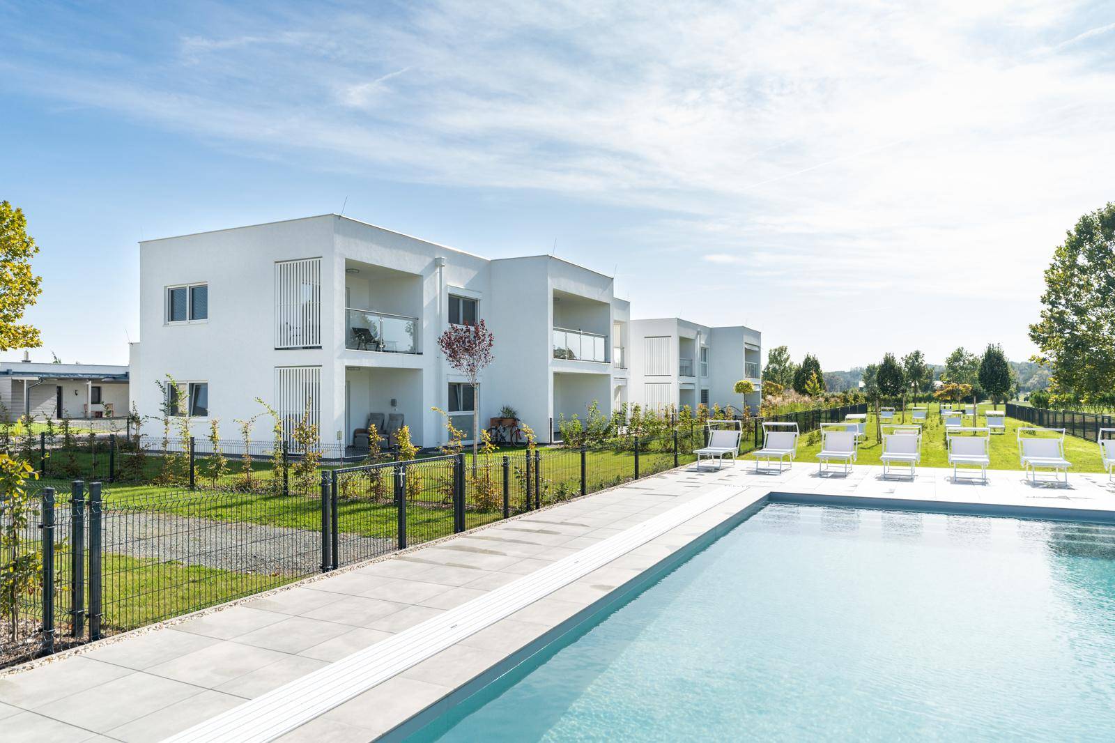Moderne Wohngebäude mit Gemeinschaftspool und Liegewiese unter blauem Himmel.