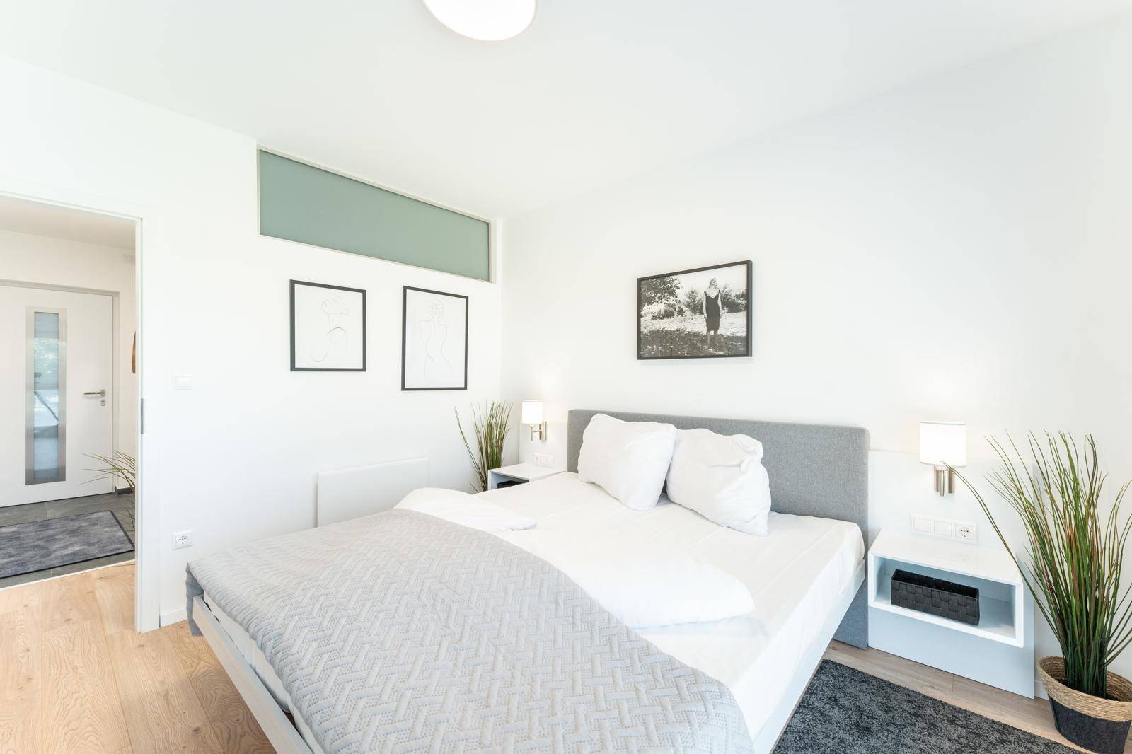 Helles Schlafzimmer mit Doppelbett, Holzboden und dezenter Wandgestaltung.