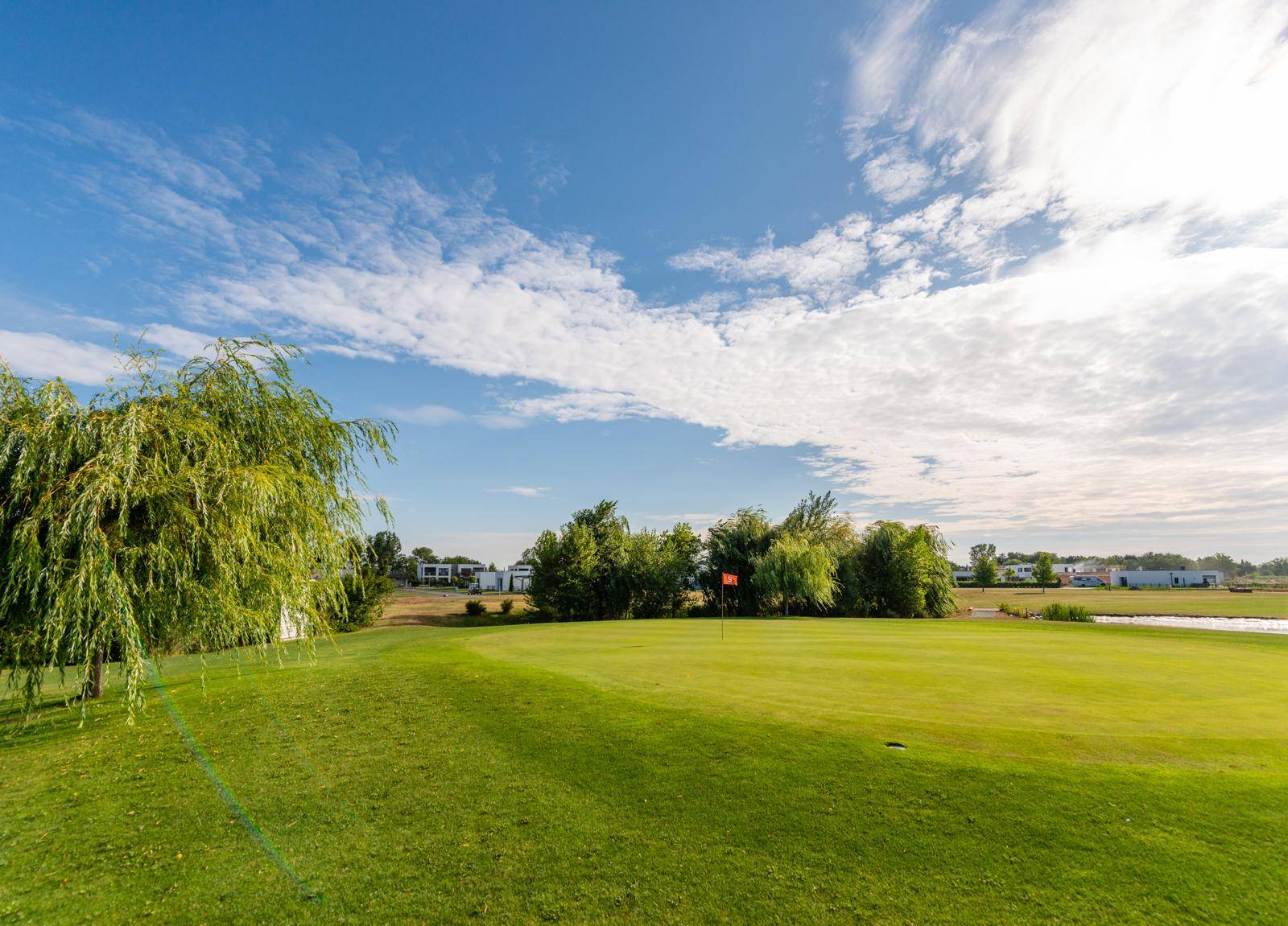 Weitläufiger Golfplatz mit gepflegtem Grün und Bäumen unter einem strahlend blauen Himmel.