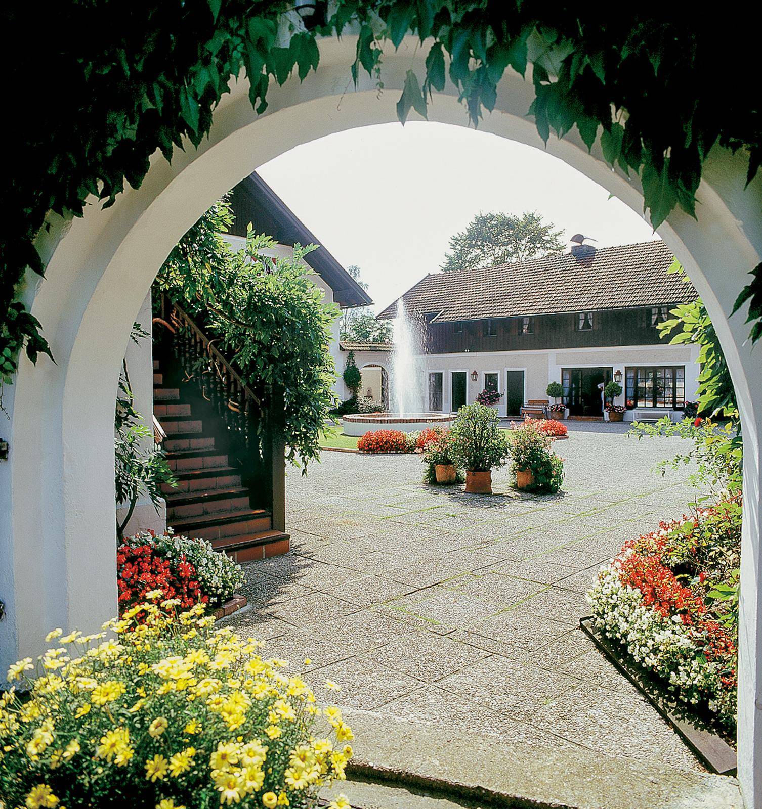 Sonniger Innenhof mit Springbrunnen, Blumenbeeten und traditioneller Architektur.