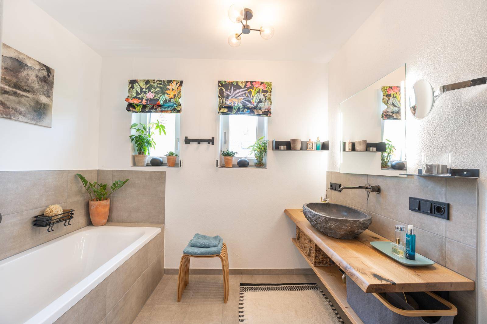 Geräumiges Badezimmer mit Badewanne, Natursteinwaschbecken und zwei Fenstern.