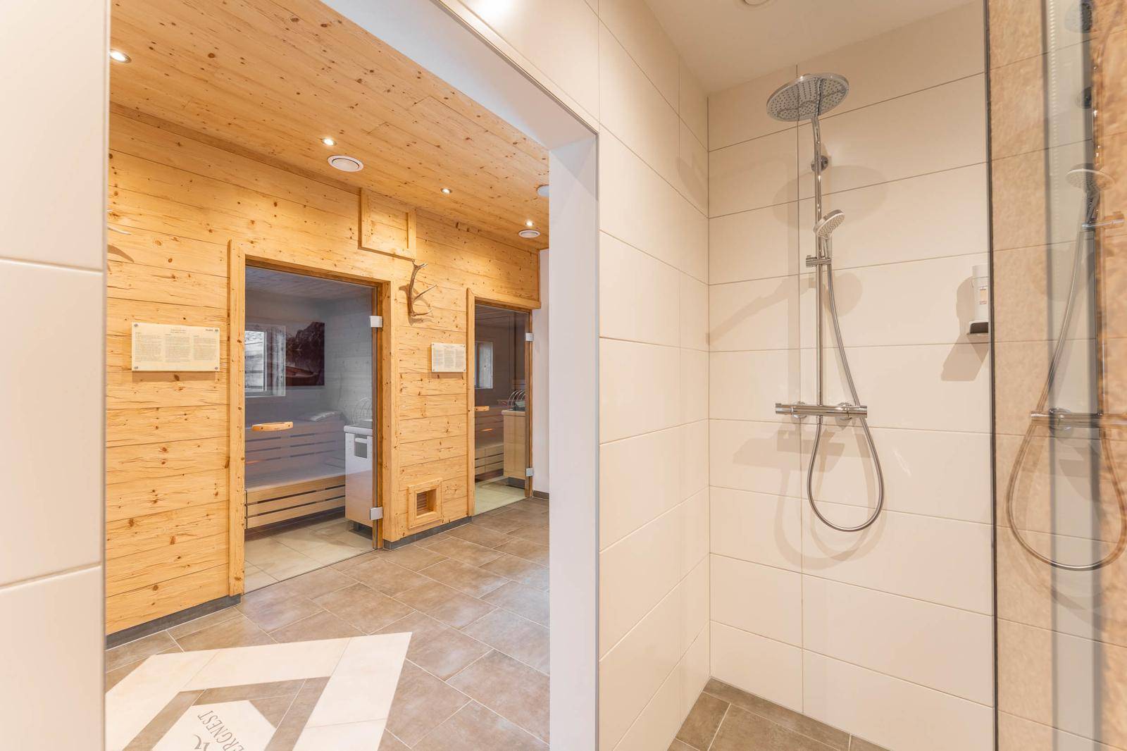Moderner Duschbereich mit weißen Fliesen und Zugang zu den Saunen im Wellnessbereich.