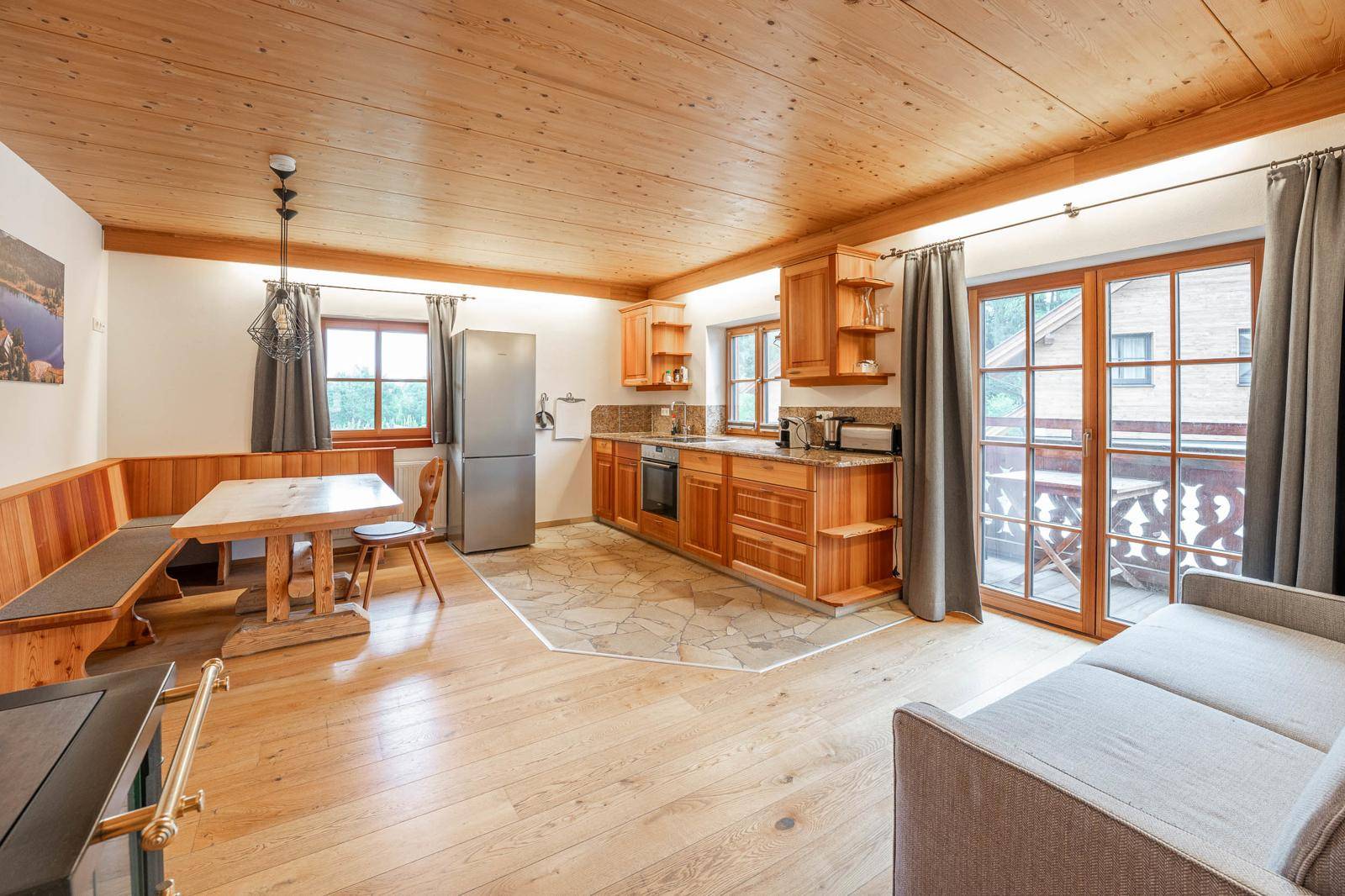 Gemütlicher Wohn-Essbereich mit Holzbalkendecke, integrierter Küche und Zugang zum Balkon.