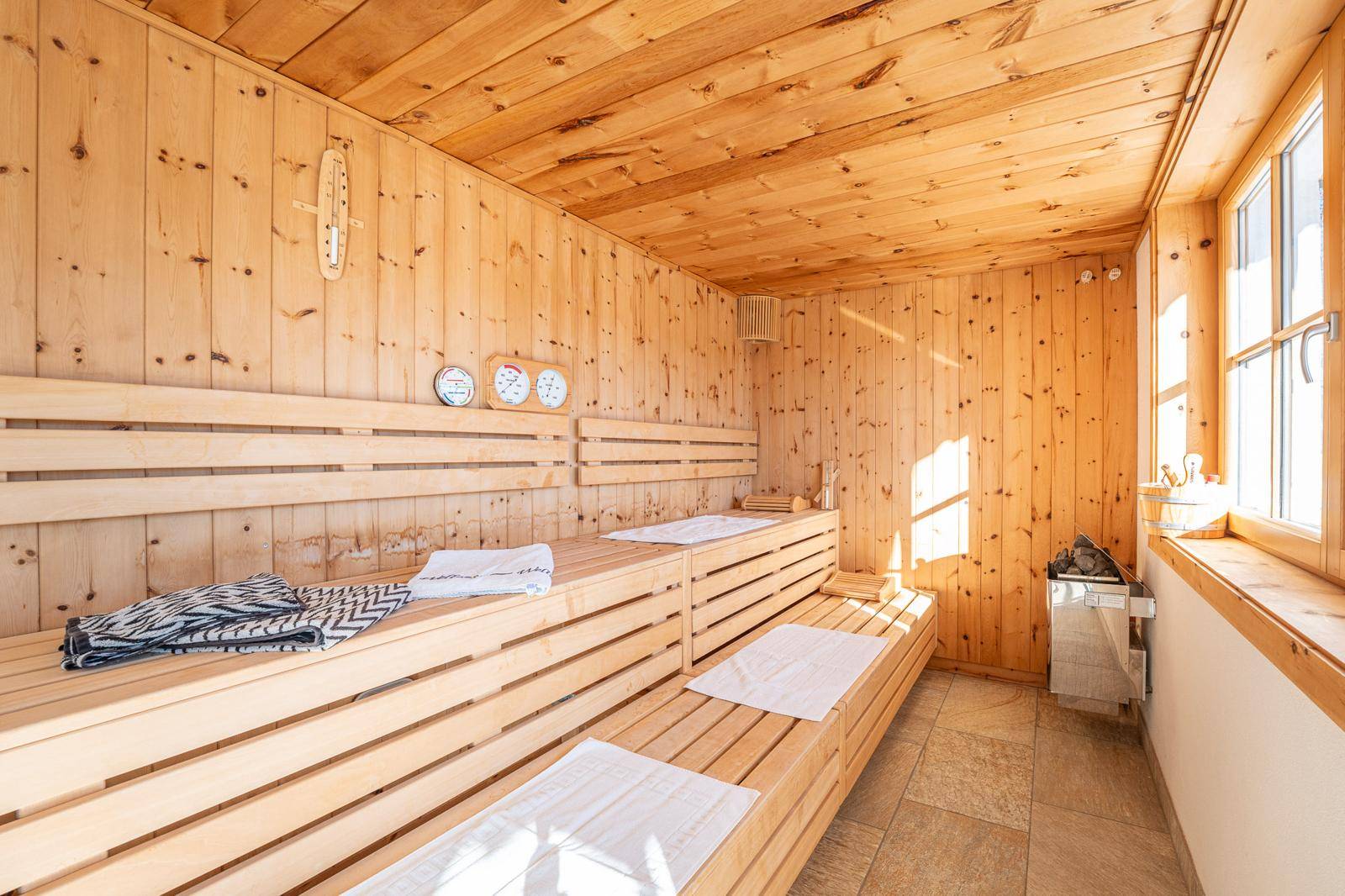 Geräumige Holzsauna mit mehreren Bänken und großem Fenster für natürliche Belichtung.
