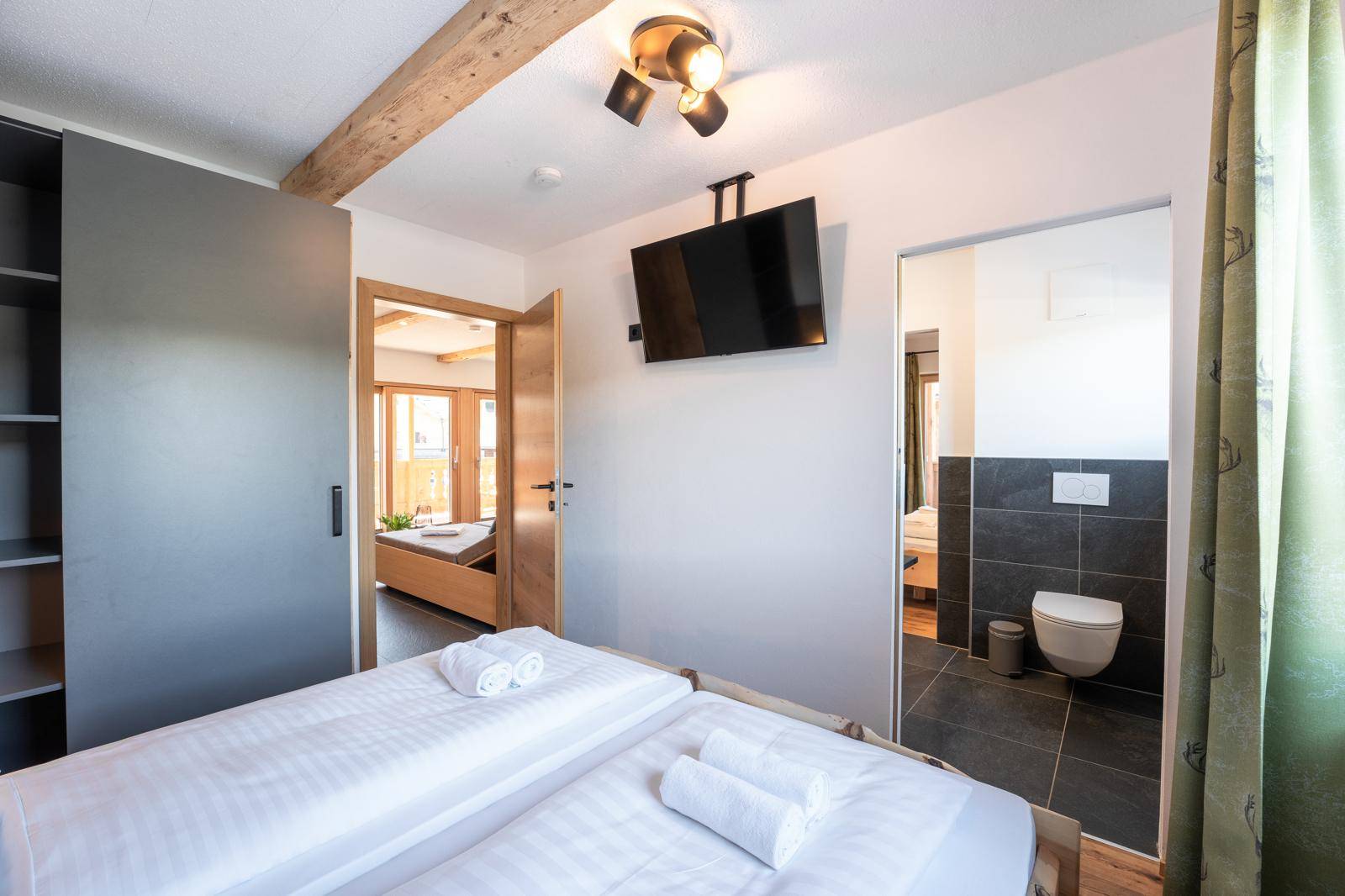 Schlafzimmer mit Holzbett, Fernseher und Zugang zu einem weiteren Raum und Bad.