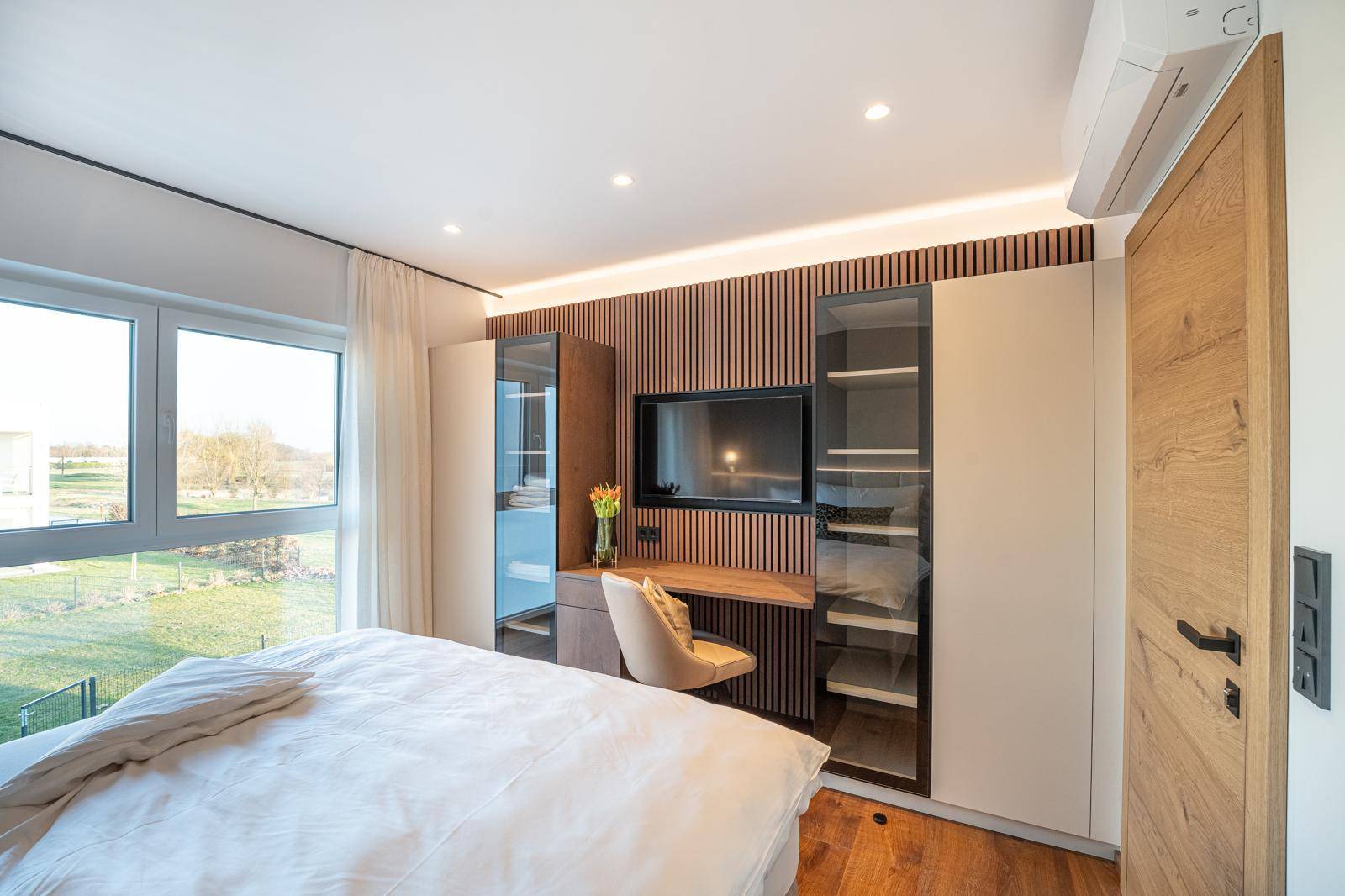 Helles Schlafzimmer mit Arbeitsbereich, Einbauschränken und Blick ins Grüne.
