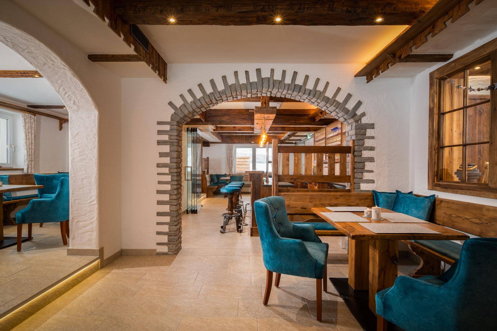 Gemütlicher Essbereich im alpinen Stil mit Holztischen, blauen Stühlen und rustikalen Steinbögen.