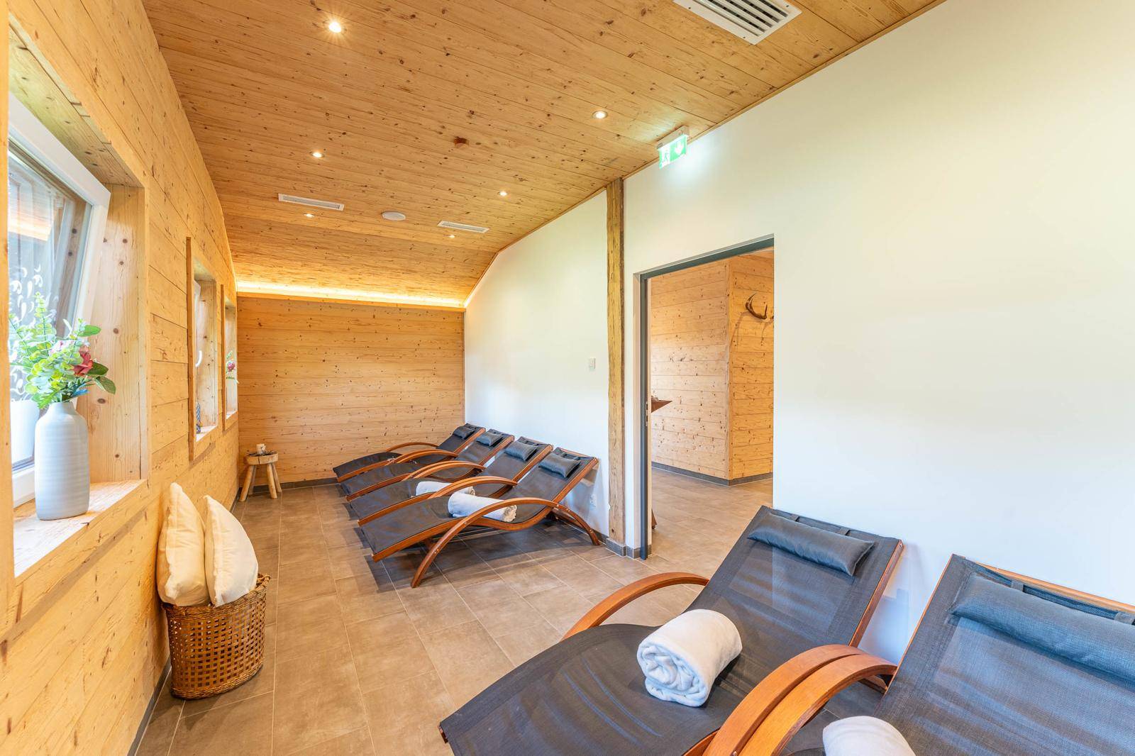 Entspannungsbereich mit Holzverkleidung, bequemen Liegen und natürlichem Lichteinfall durch Fenster.