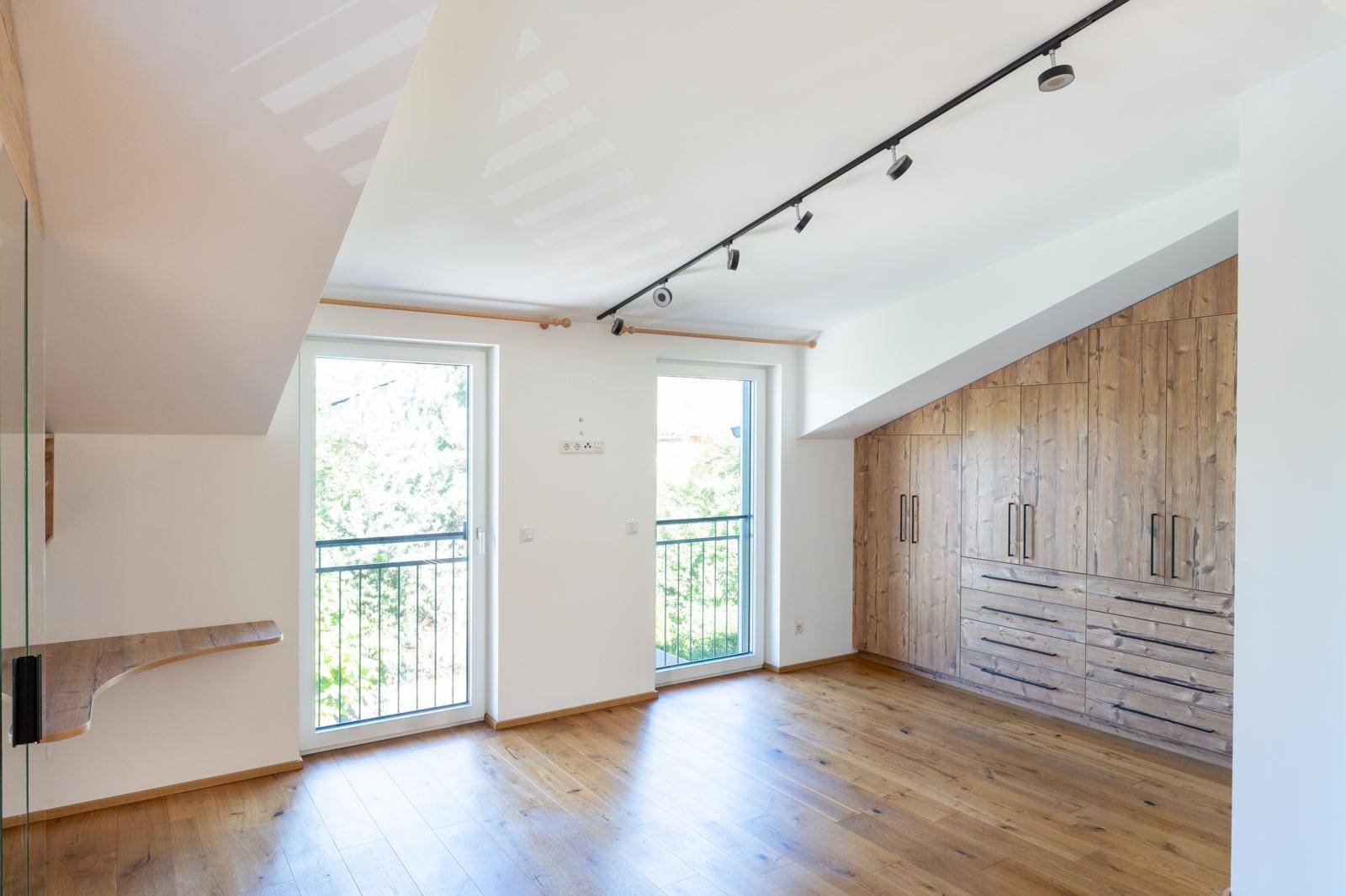 Schlafzimmer mit Dachschräge, Holzboden, Einbauschränken und französischen Balkonen.