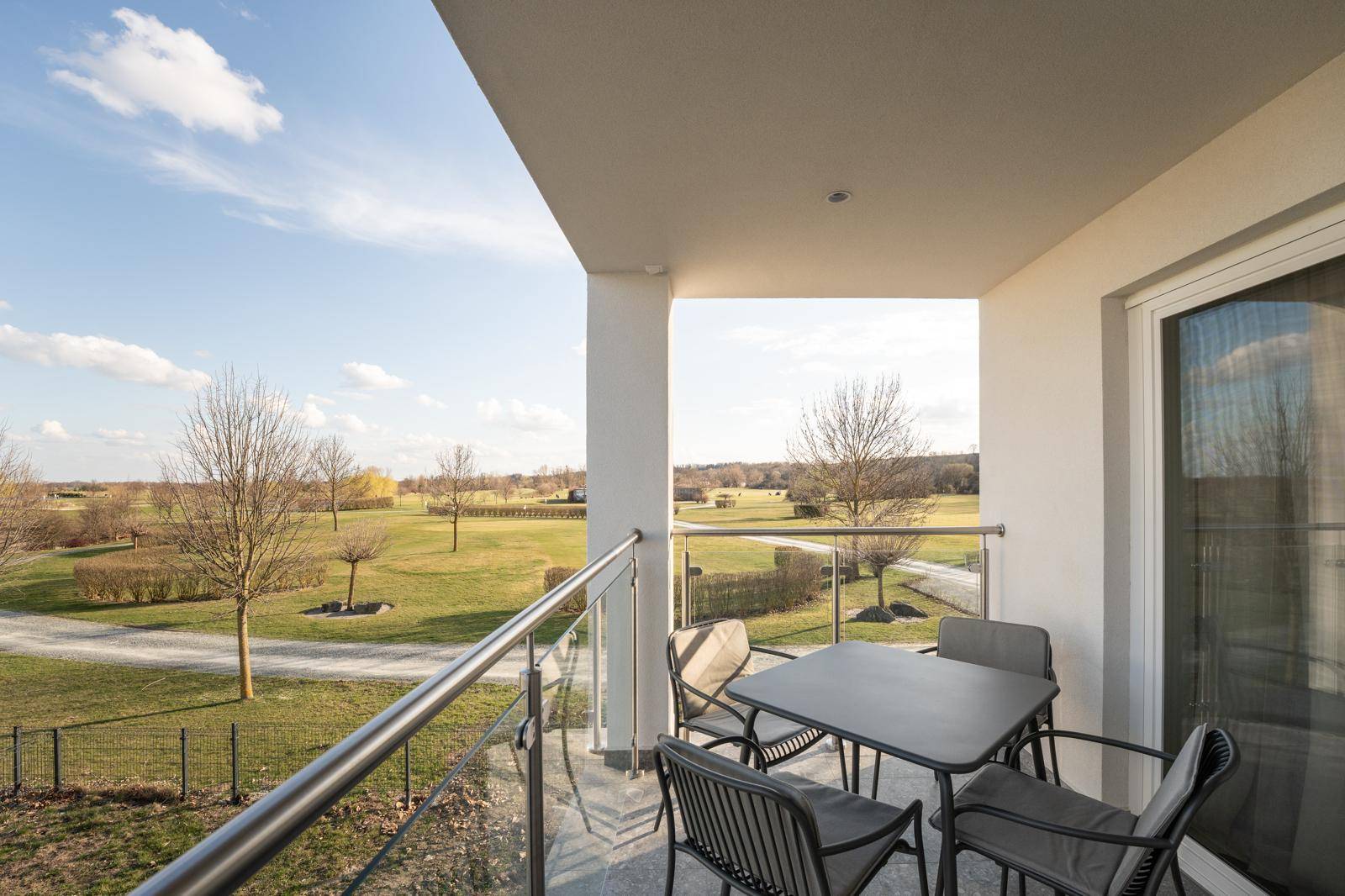 Geräumiger Balkon mit Sitzgelegenheiten und weitem Blick ins Grüne unter blauem Himmel.