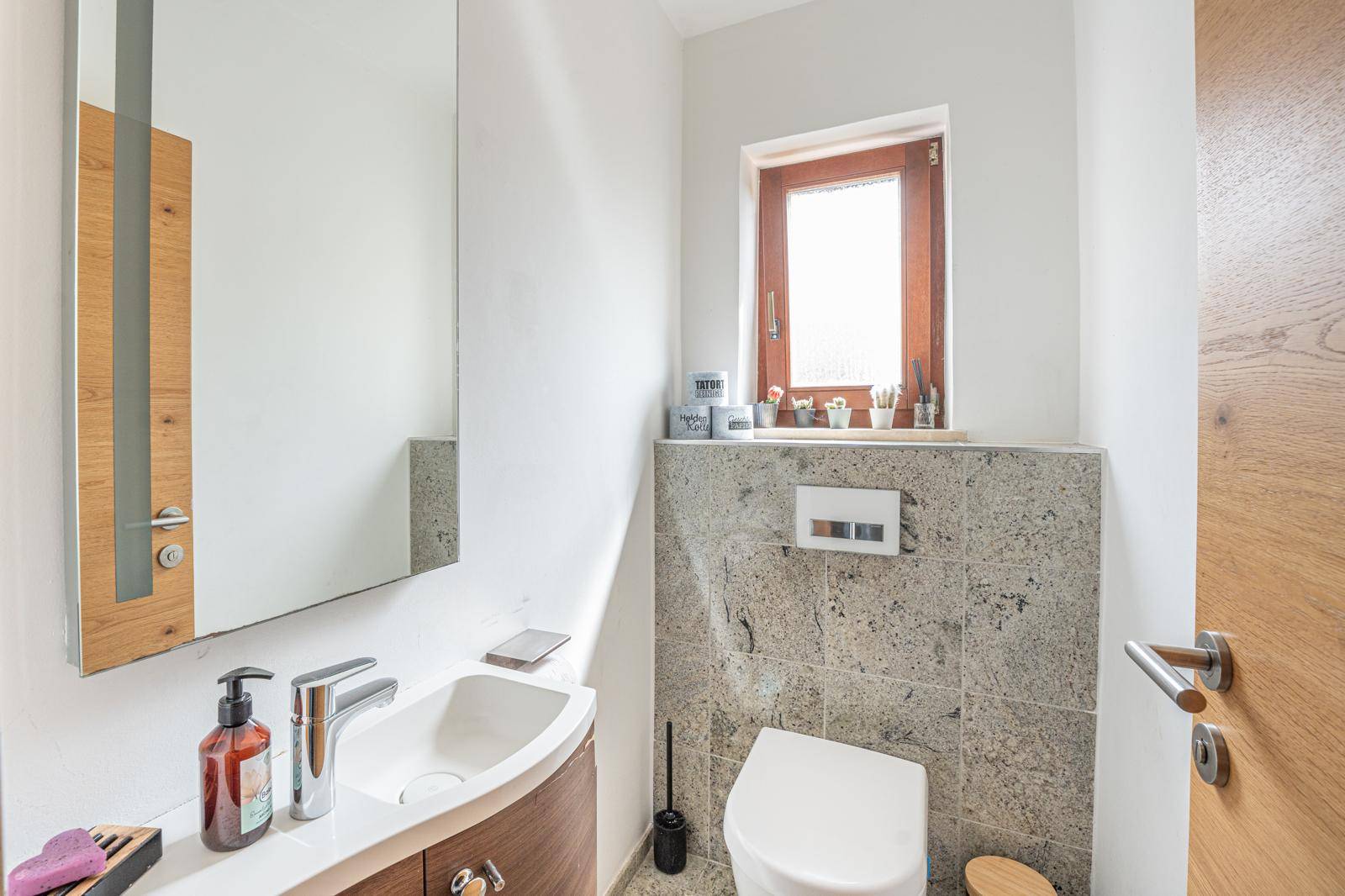 Modernes Gäste-WC mit Fenster, Wand-WC und stilvollem Waschbecken in heller Farbgebung.