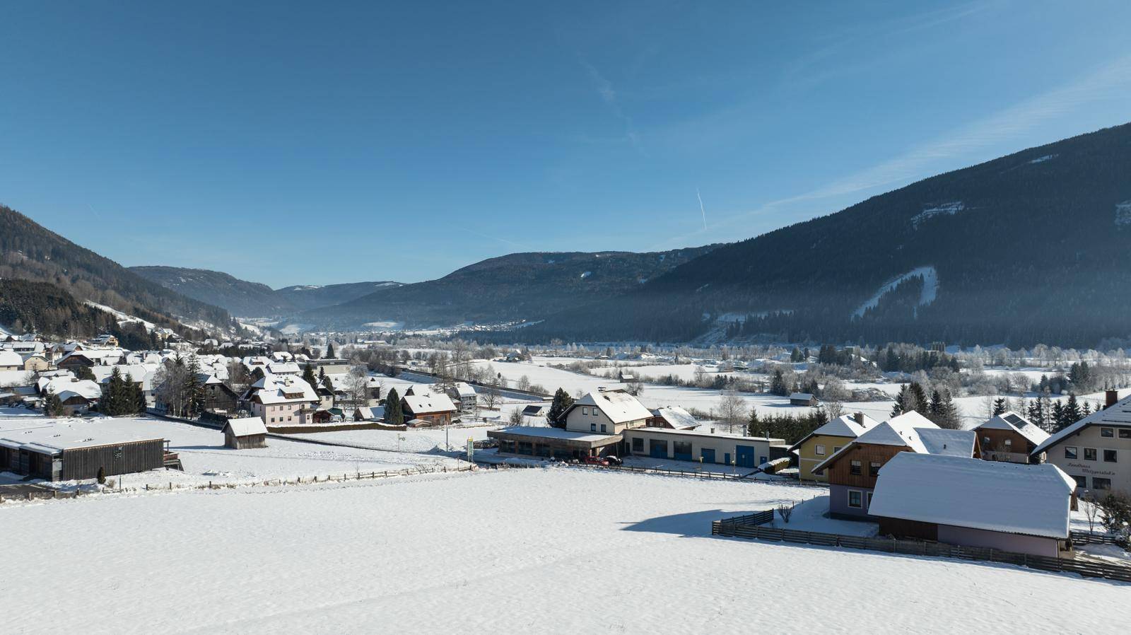 Idyllischer Ausblick auf ein schneebedecktes Tal mit verstreuten Häusern und einer weiten Naturlandschaft.