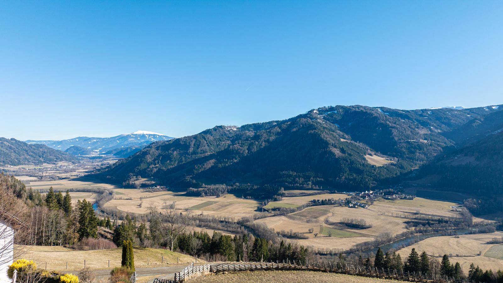 Panoramablick auf die weite Berglandschaft mit Tälern und Wäldern unter blauem Himmel.