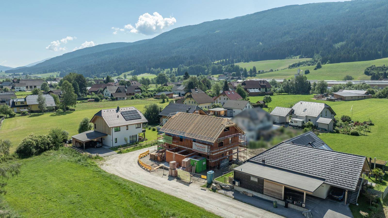 Baustelle eines Einfamilienhauses im Rohbau mit Dachstuhl und Blick auf die Berglandschaft.