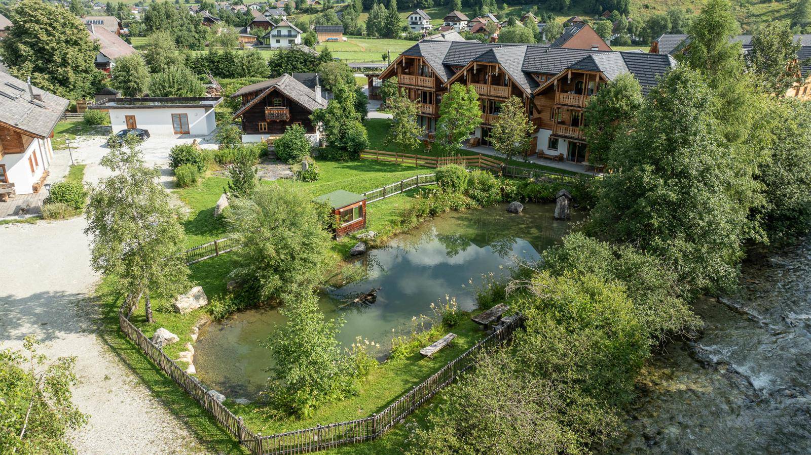 Idyllischer Gartenbereich mit Teich, umgeben von Bäumen und grüner Landschaft.