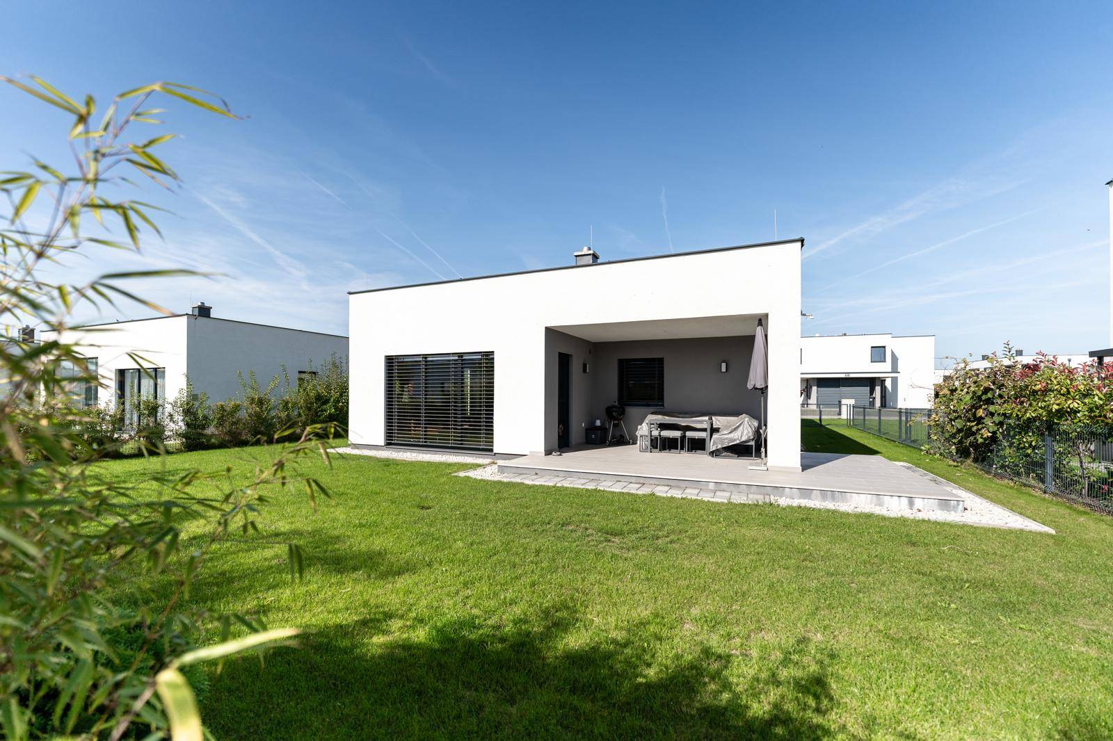 Rückansicht eines modernen Hauses mit großer Rasenfläche und überdachter Terrasse für entspannte Stunden.