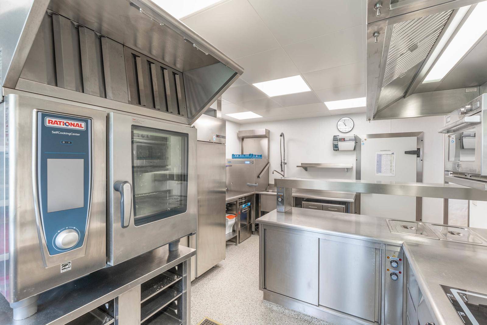 Moderne Großküche mit professionellen Kochgeräten, Edelstahloberflächen und effizienter Beleuchtung.