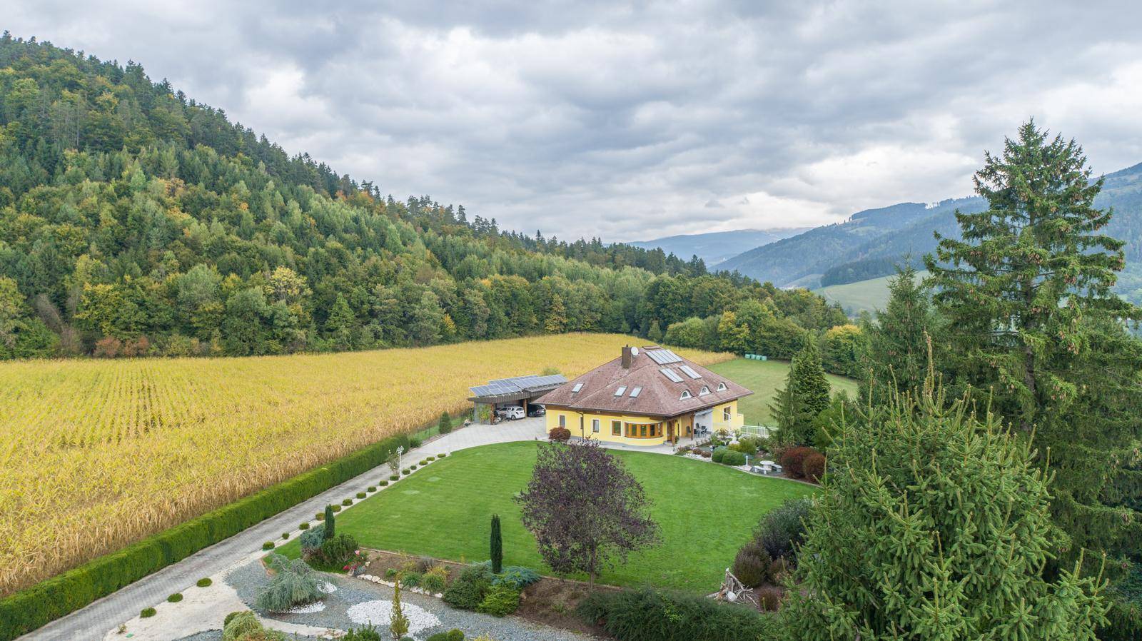 Panoramablick auf das gelbe Haus, eingebettet in eine grüne Hügellandschaft mit weiten Feldern.