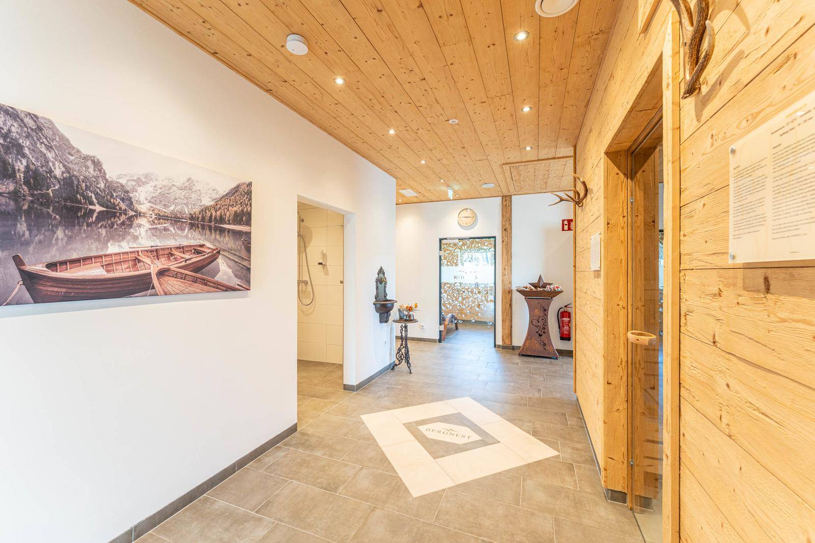 Heller Flur im Wellnessbereich mit Holzelementen, Fliesenboden und dekorativen Bildern.
