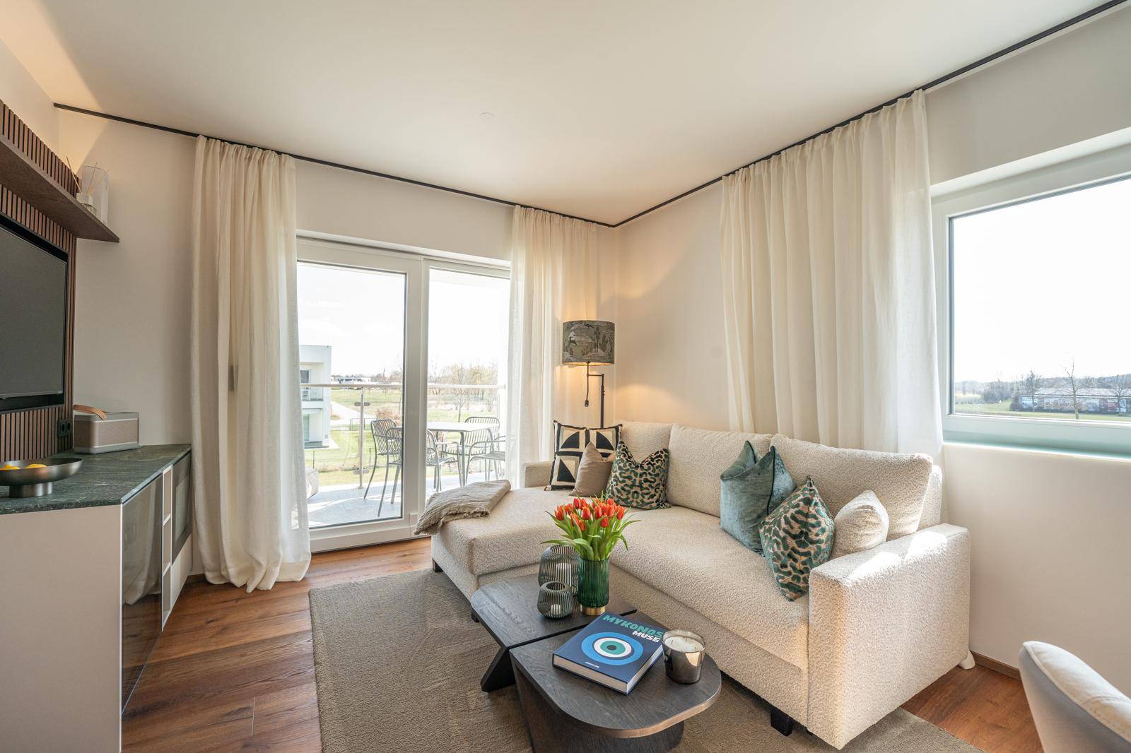 Lichtdurchflutetes Wohnzimmer mit Balkonzugang, bequemer Couch und Blick ins Freie.