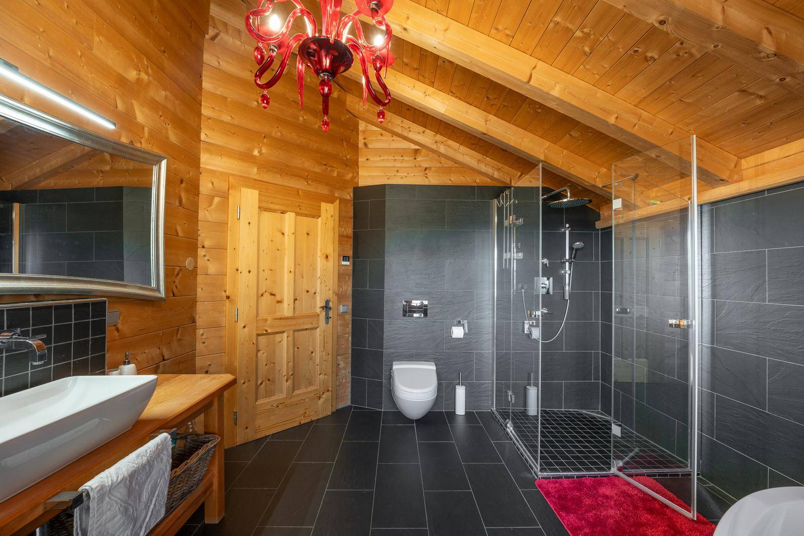 Modernes Badezimmer mit ebenerdiger Dusche, dunklen Fliesen, Holzwänden und Wand-WC.