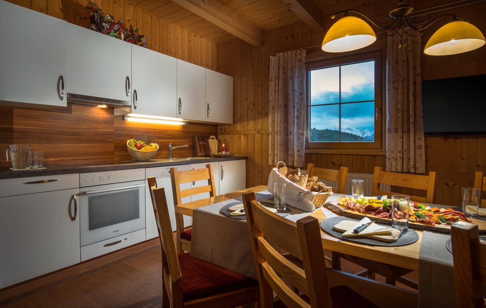 Rustikale Küche mit Holzwänden, weißer Einbauküche und Esstisch mit Bergblick.