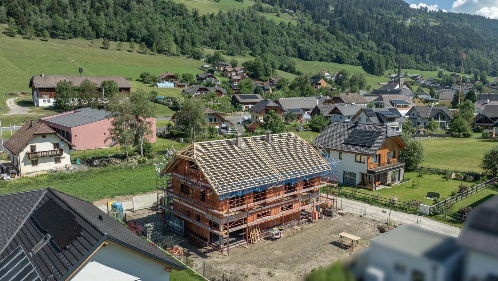 Neubau im Rohbau mit Dachstuhl, eingebettet in eine ländliche Siedlung mit Bergblick.