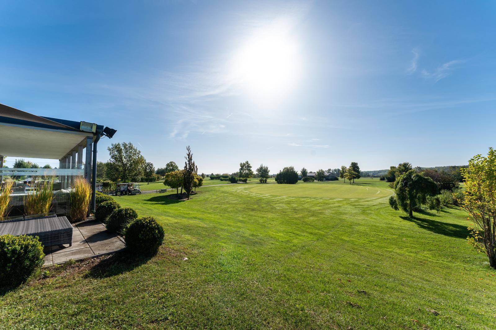 Weitläufiger Golfplatz unter strahlendem Sonnenschein mit gepflegten Grüns und Bäumen.