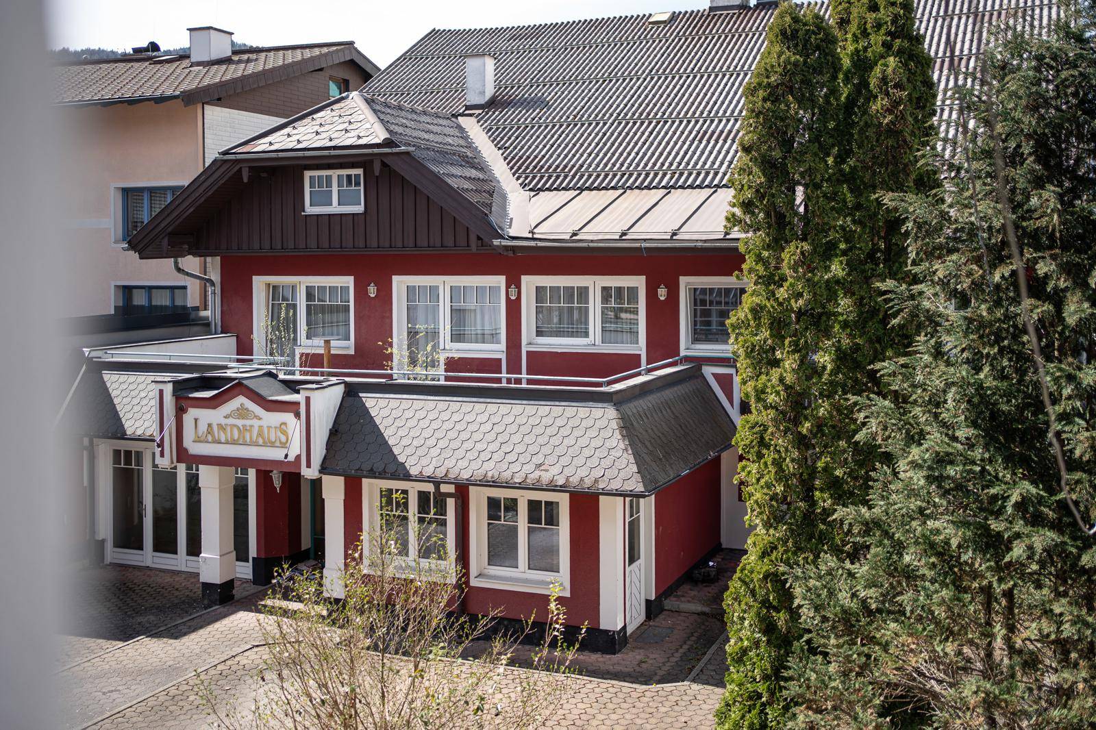 Kleineres rotes Landhaus mit traditionellem Dach und weißen Fenstern, umgeben von Bäumen.