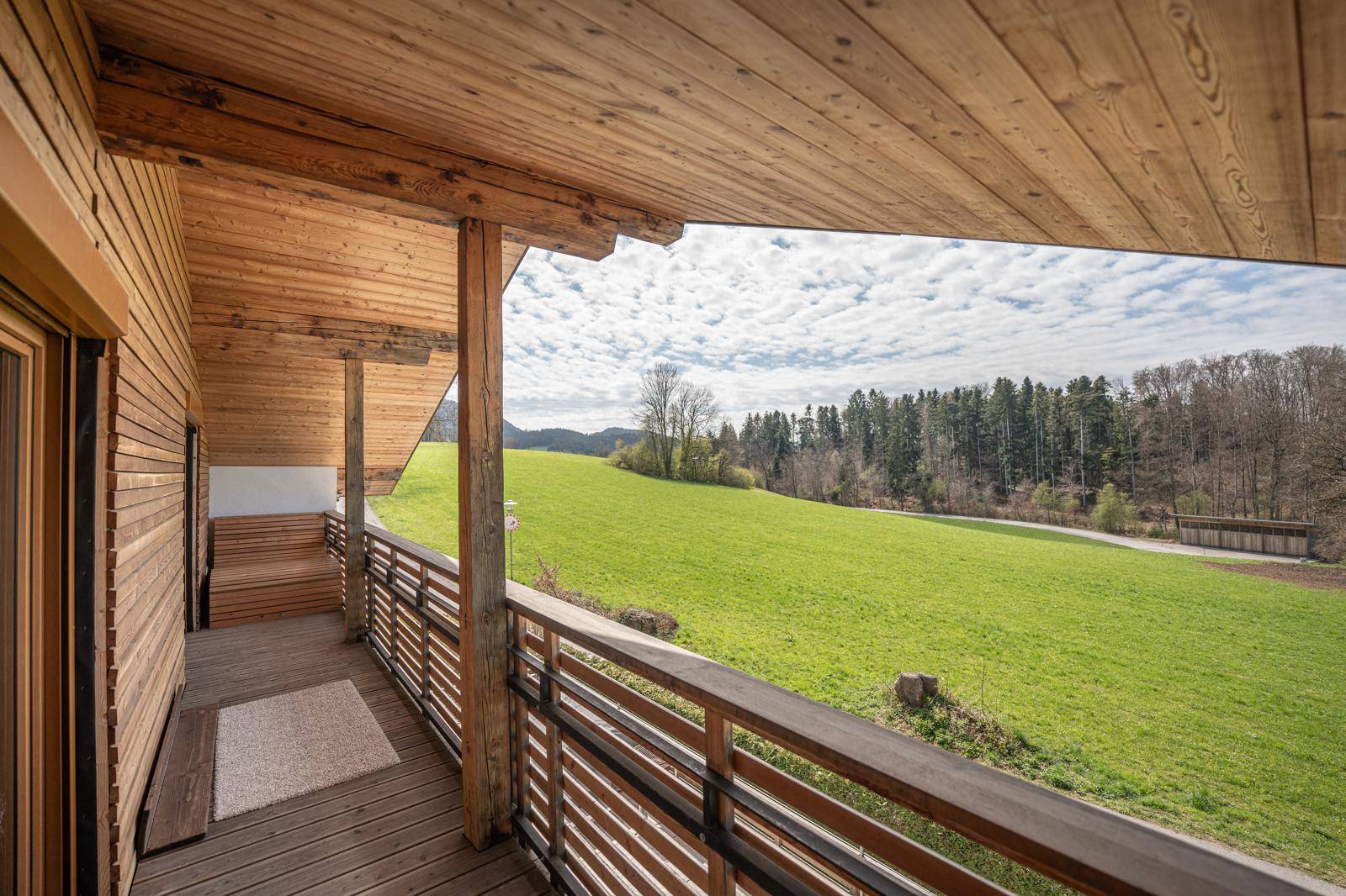Langer Holzbalkon mit Sitzbank und Panoramablick auf die idyllische Landschaft, perfekt für sonnige Tage.