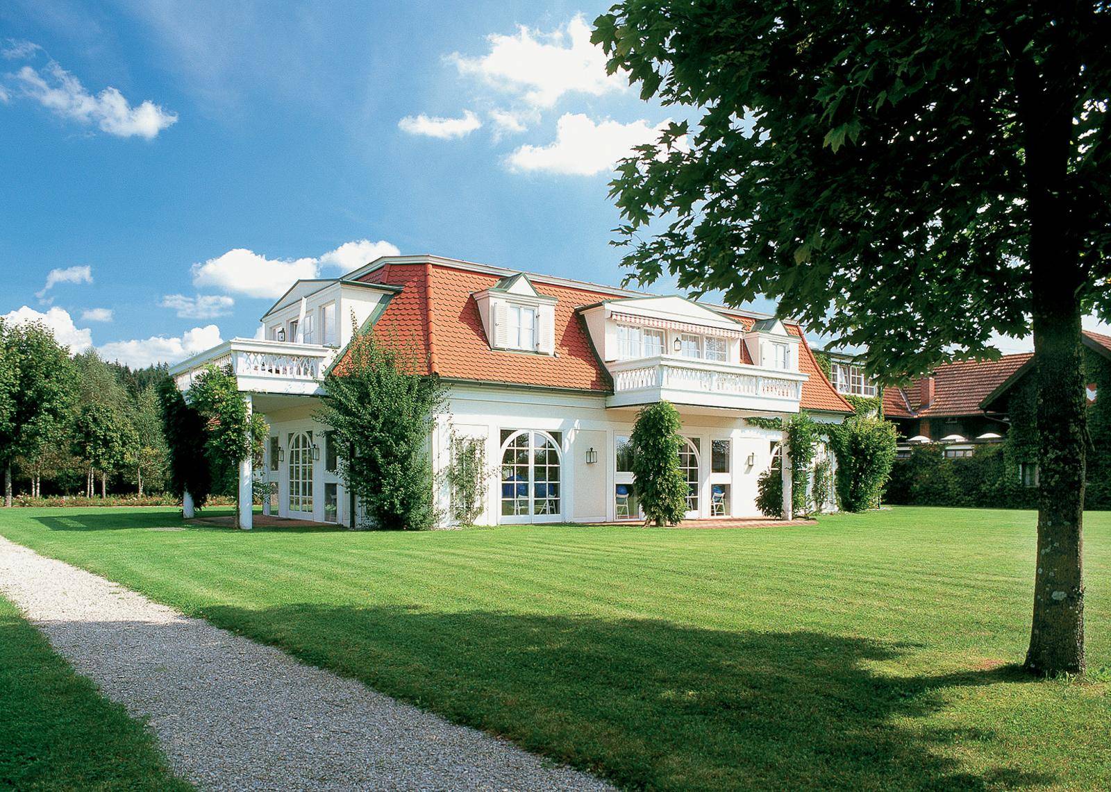 Großer Garten mit Rasenfläche und eleganter Villa mit Balkonen und Mansarddach.
