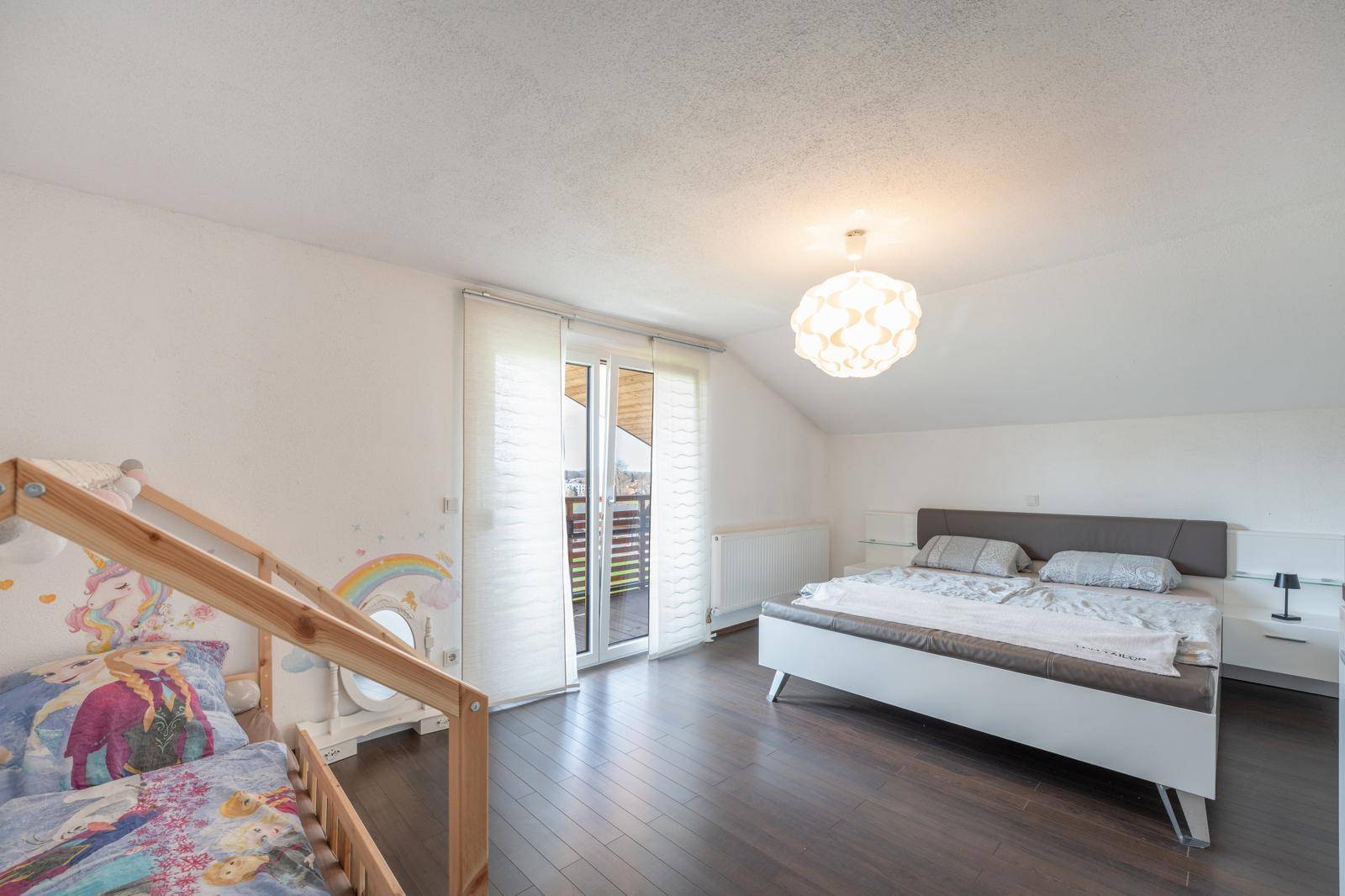 Helles Schlafzimmer mit Balkonzugang, Holzboden und modernem Doppelbett unter schräger Decke.